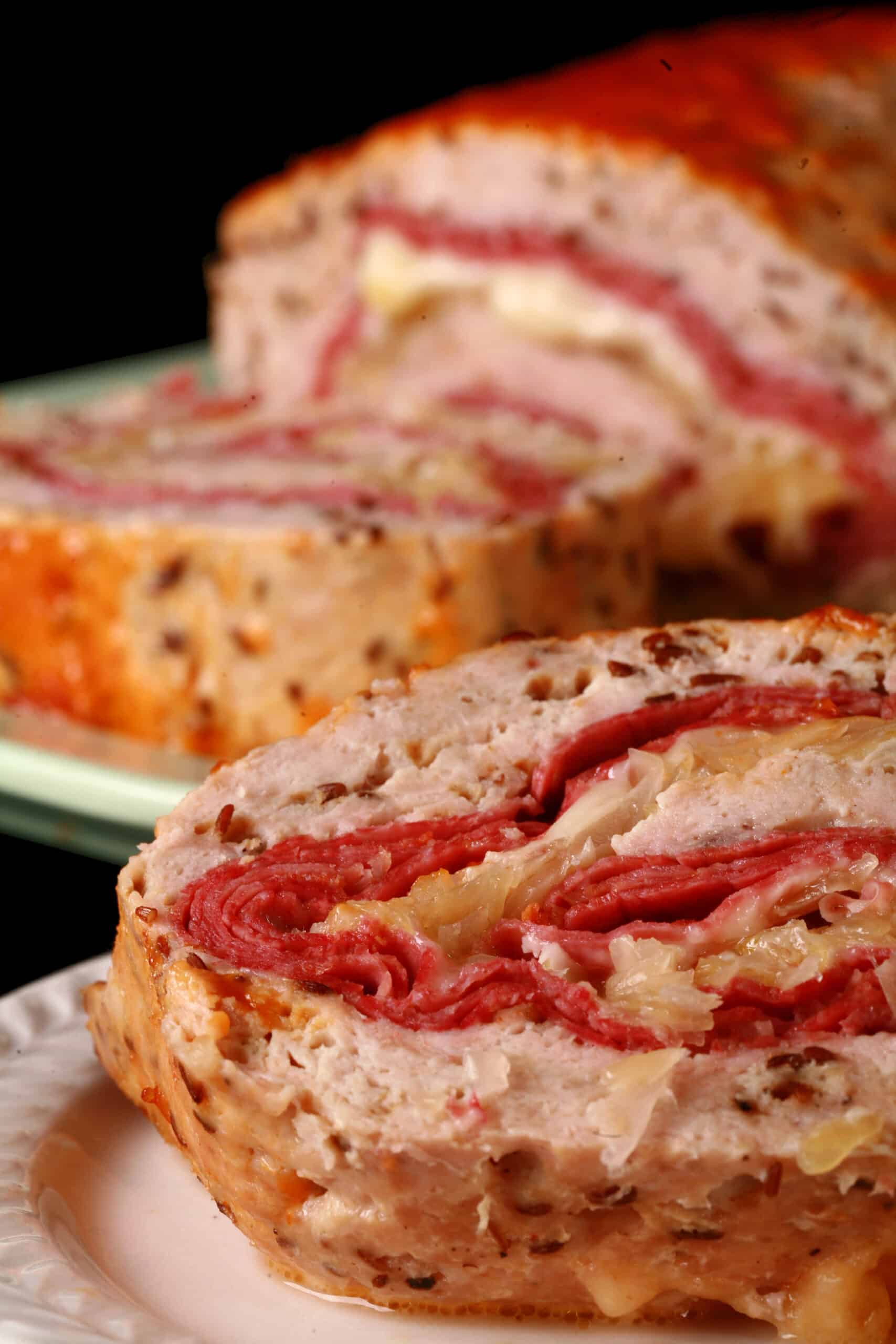 A slice of Reuben Stuffed Meatloaf on a plate in front of the rest of the reuben meatloaf.