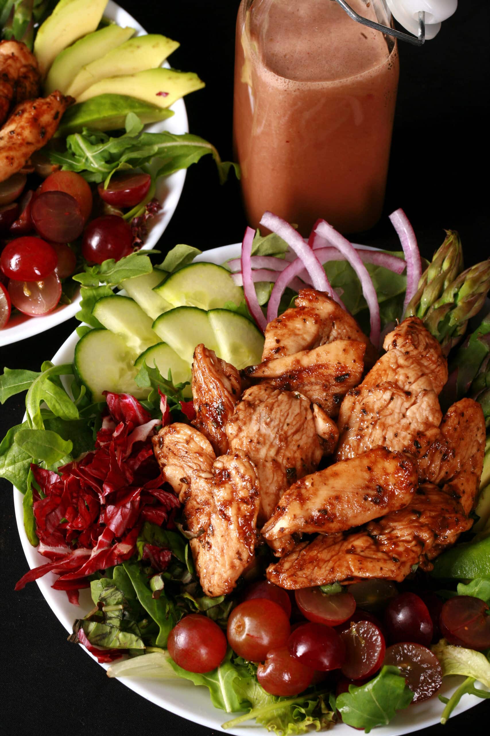 A jewel toned salad topped with balsamic glazed chicken and red grapes.