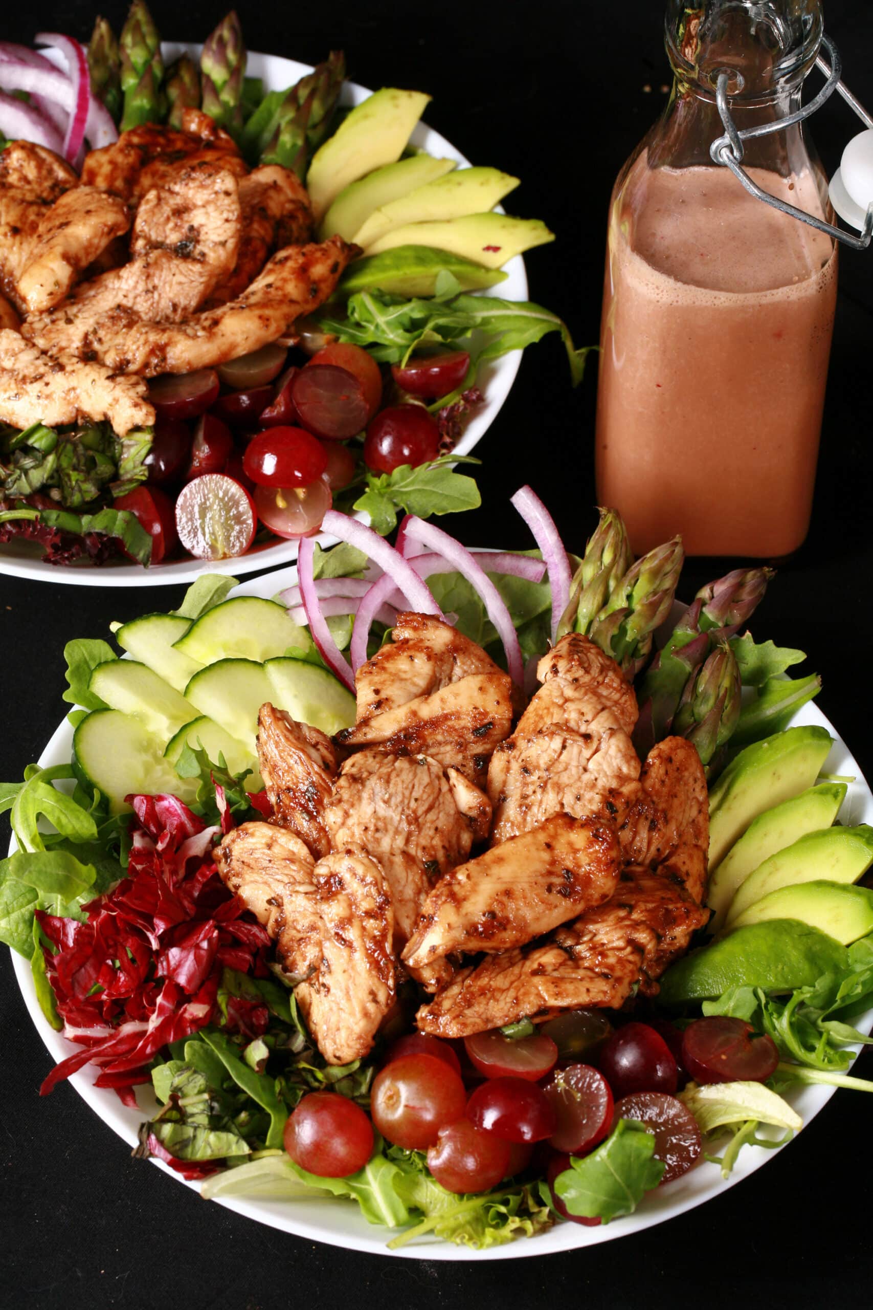 A jewel toned salad topped with balsamic glazed chicken and red grapes.