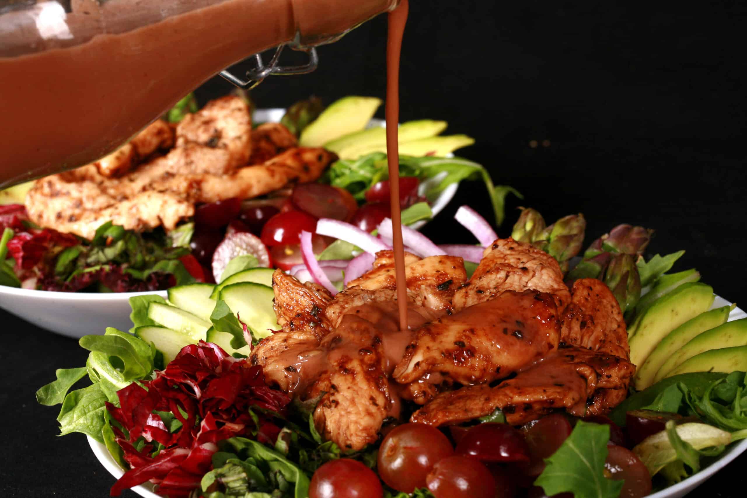 A jewel toned salad topped with balsamic glazed chicken and red grapes.