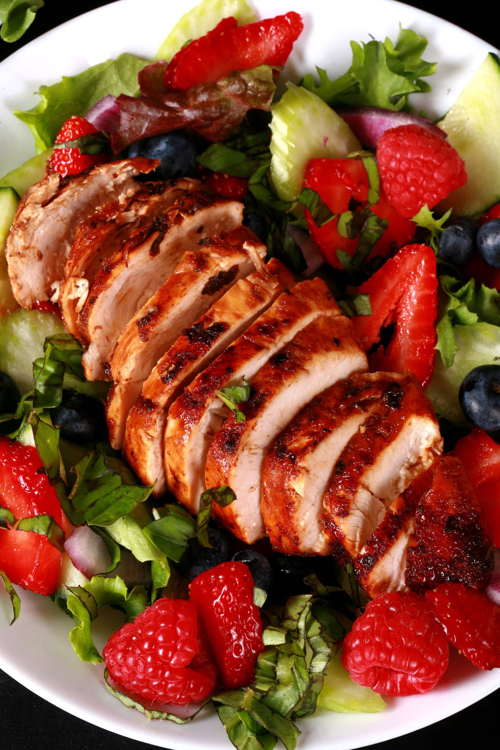 2 summer balsamic salads with balsamic glazed chicken and berries. There is a bottle of fresh raspberry balsamic vinaigrette next to it.