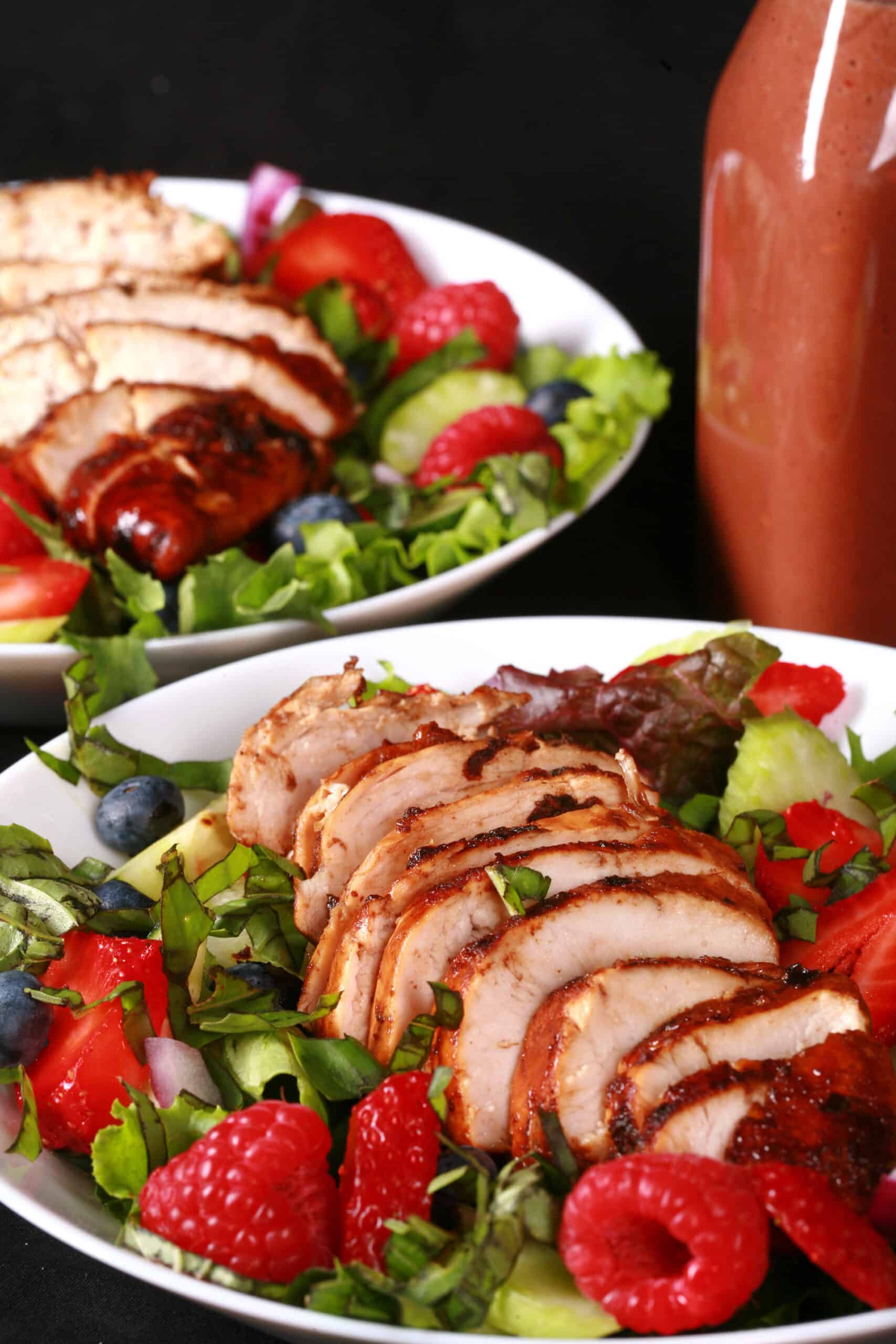 2 summer salads with balsamic glazed chicken and berries. There is a bottle of fresh raspberry balsamic vinaigrette next to it.