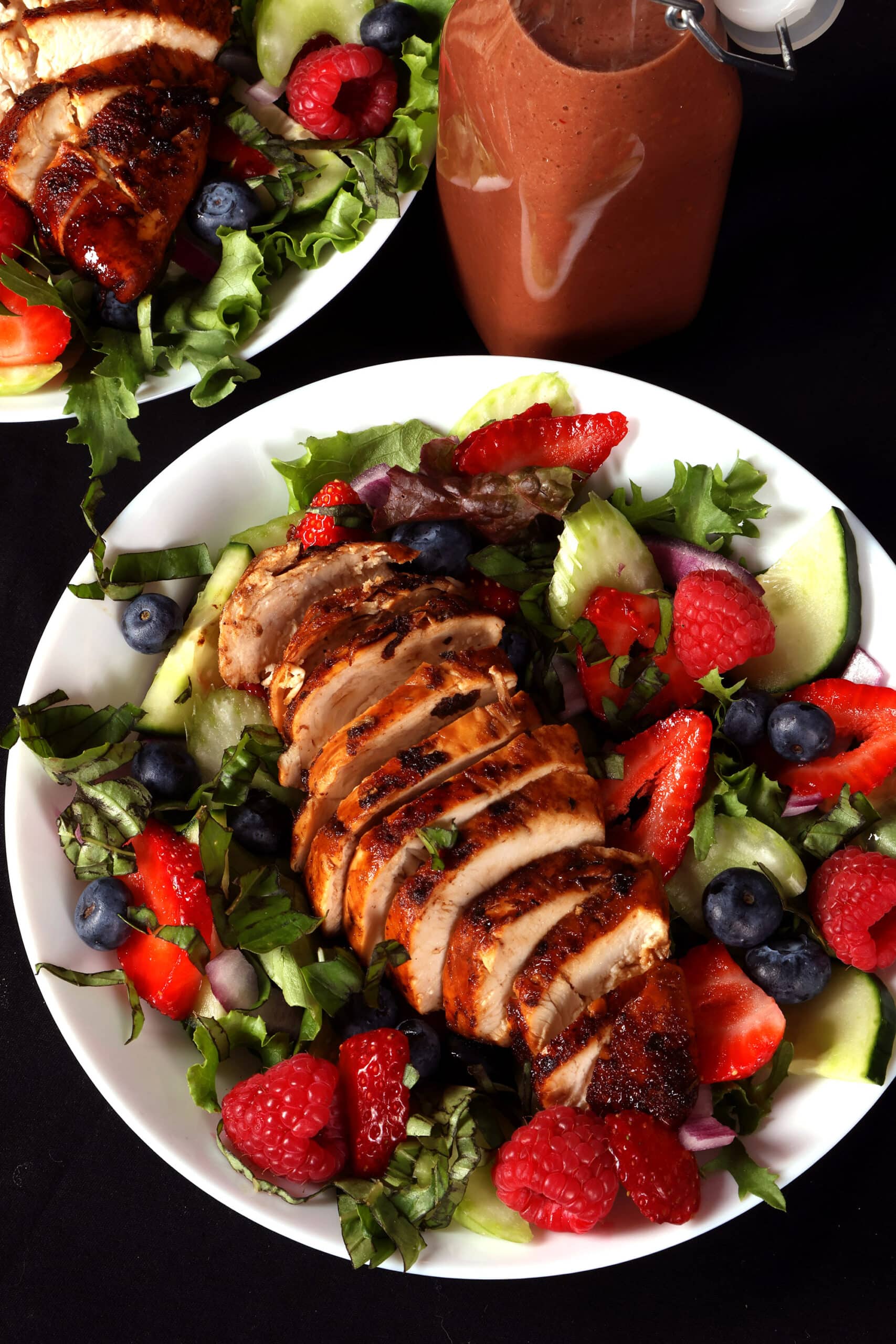 2 summer balsamic salads with balsamic glazed chicken and berries. There is a bottle of fresh raspberry balsamic vinaigrette next to it.