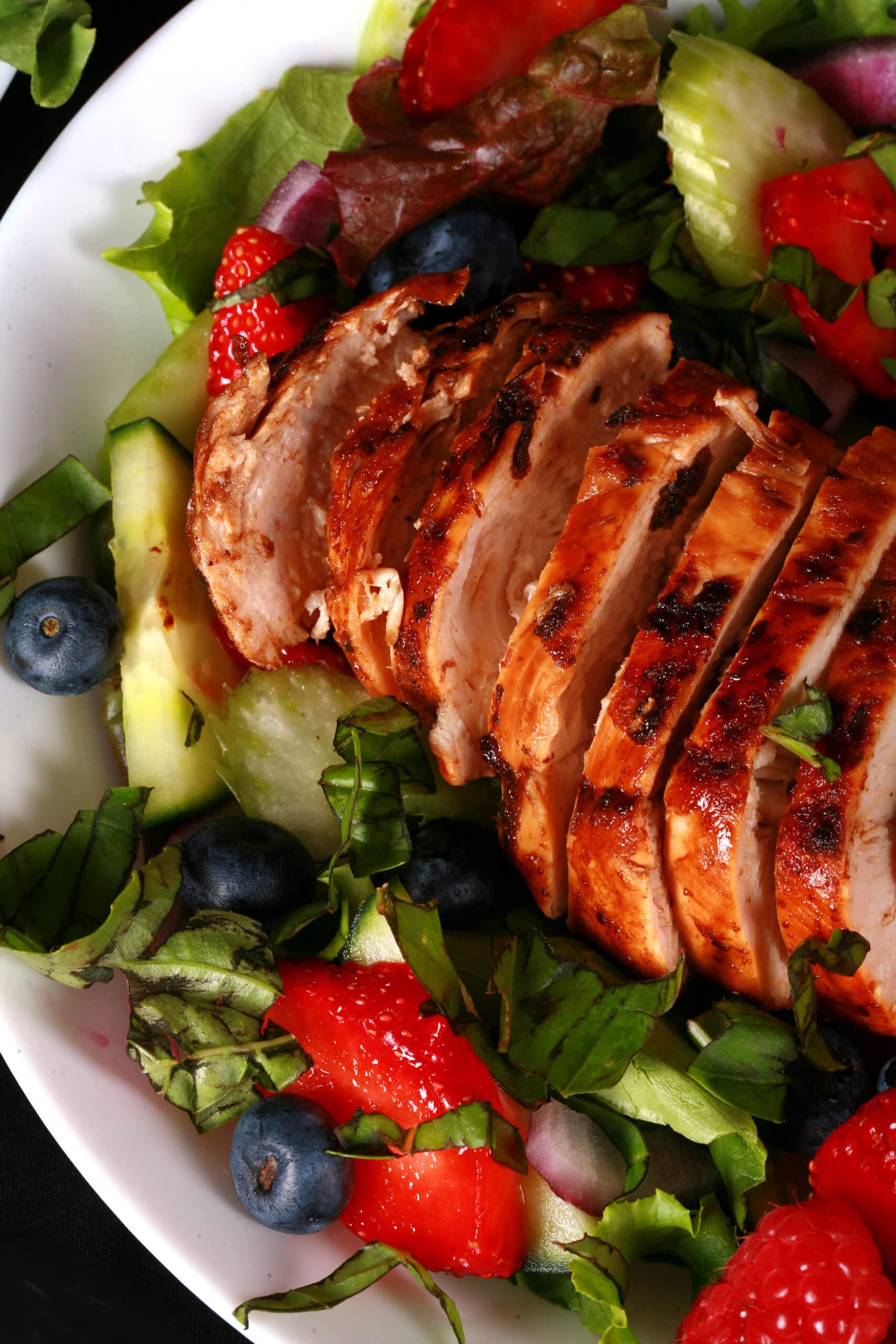 2 summer balsamic salads with balsamic glazed chicken and berries. There is a bottle of fresh raspberry balsamic vinaigrette next to it.