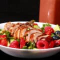 2 summer salads with balsamic glazed chicken and berries. There is a bottle of fresh raspberry balsamic vinaigrette next to it.