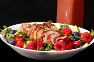 2 summer salads with balsamic glazed chicken and berries. There is a bottle of fresh raspberry balsamic vinaigrette next to it.