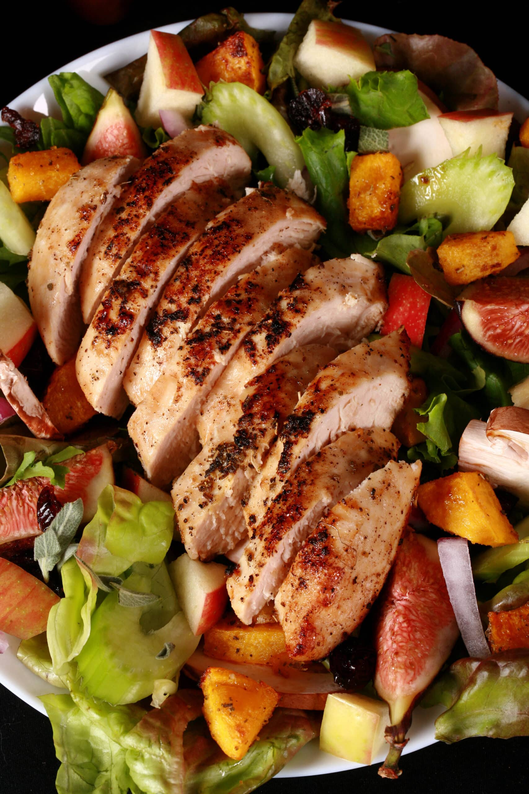 A main dish fall chicken salad with apples, roasted squash, figs, and more. There is a bottle of maple balsamic vinaigrette.