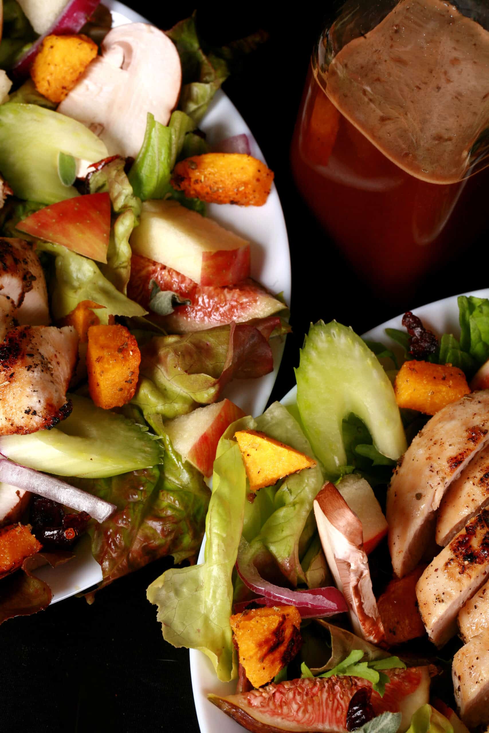 A harvest chicken salad with apples, roasted squash, figs, and more. There is a bottle of maple balsamic vinaigrette.