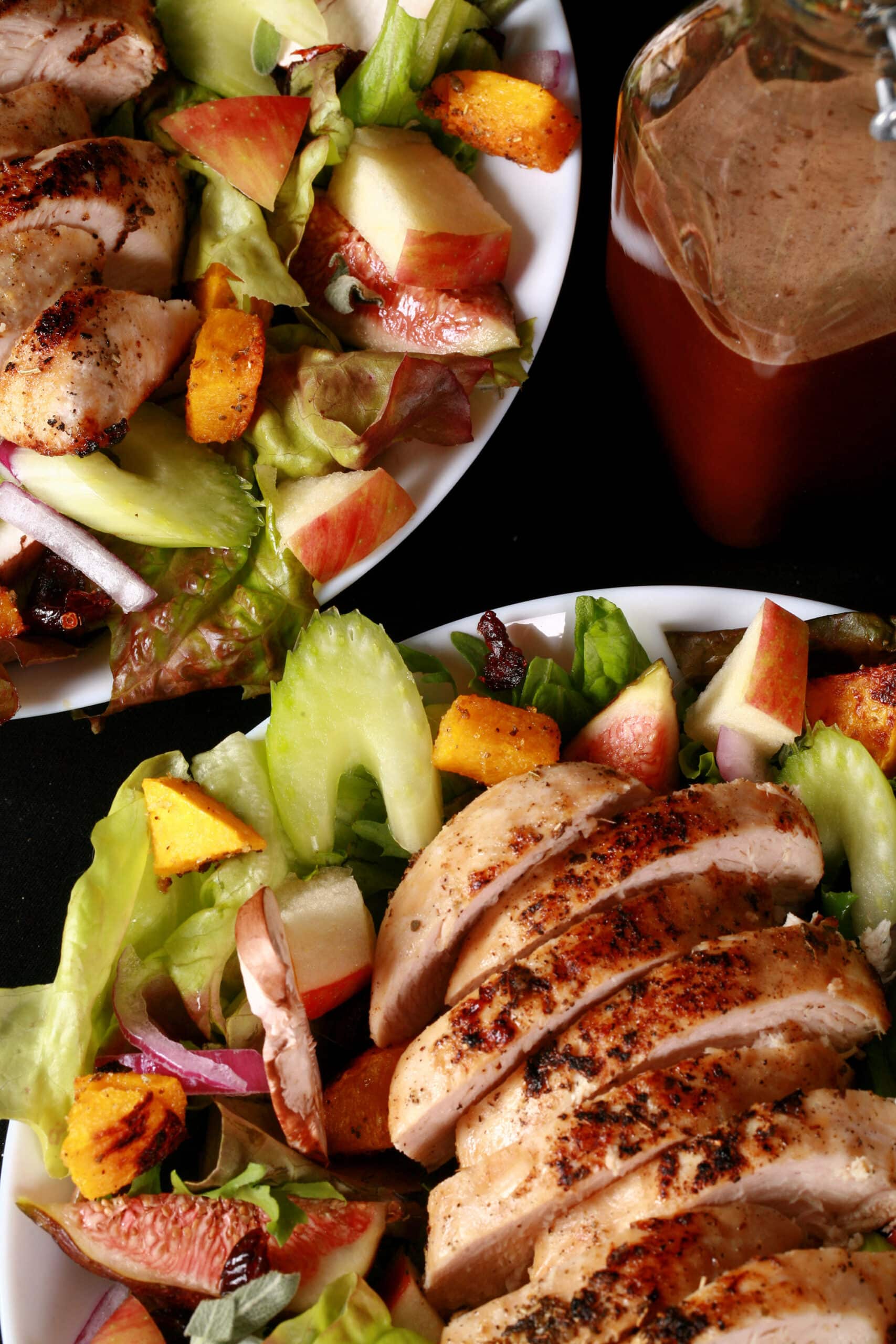 A main dish fall chicken salad with apples, roasted squash, figs, and more. There is a bottle of maple balsamic vinaigrette.