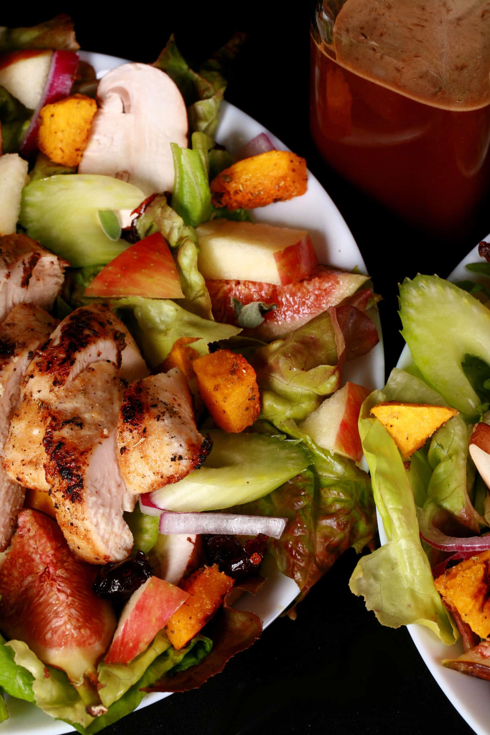 A harvest chicken salad with apples, roasted squash, figs, and more. There is a bottle of maple balsamic vinaigrette.