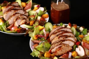 A harvest chicken salad with apples, roasted squash, figs, and more. There is a bottle of maple balsamic vinaigrette.