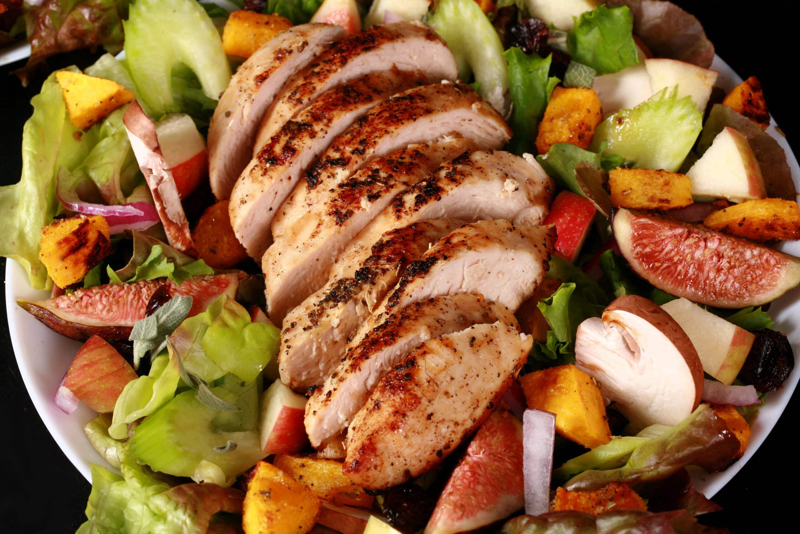 A main dish fall chicken salad with apples, roasted squash, figs, and more. There is a bottle of maple balsamic vinaigrette.