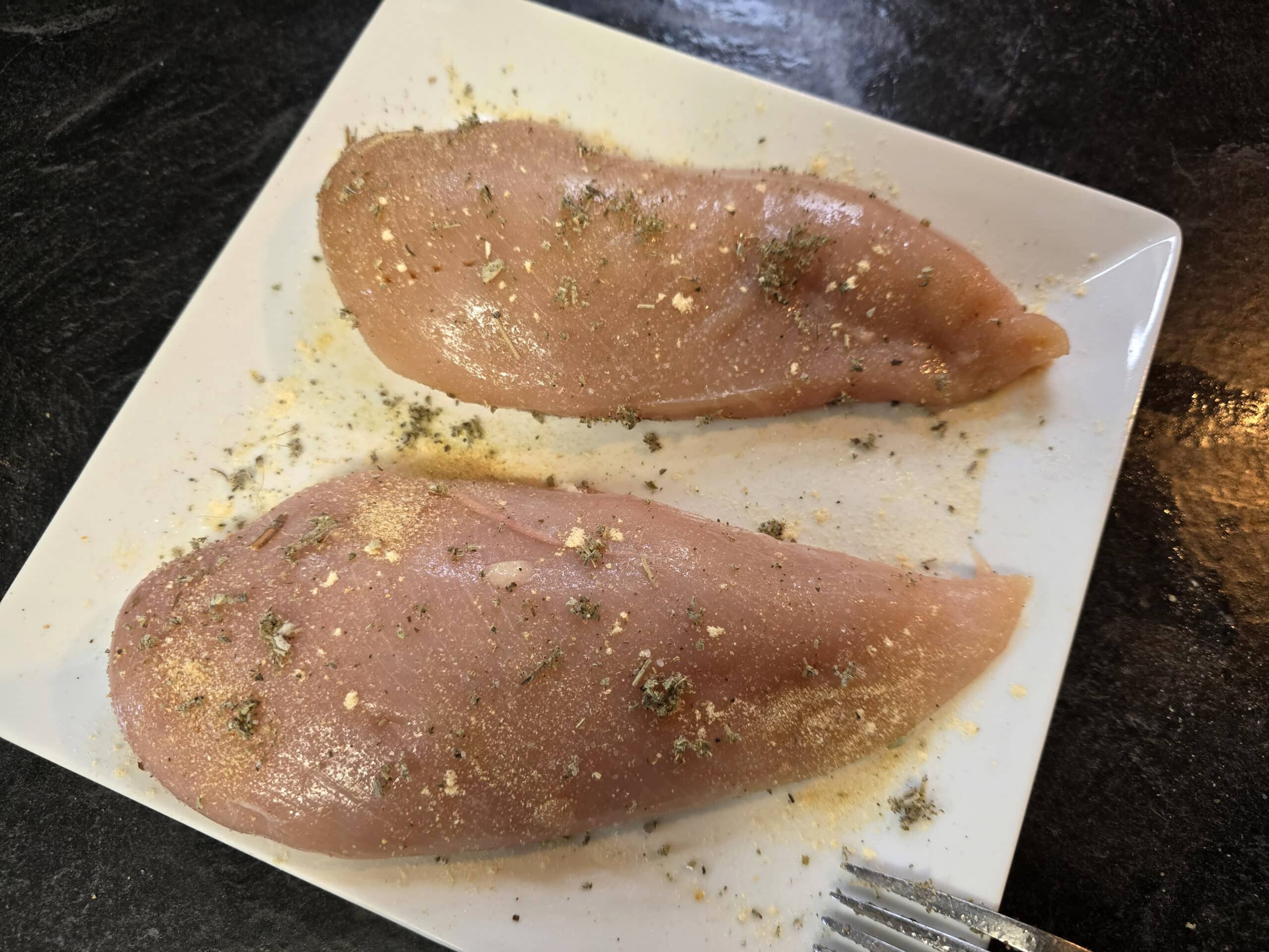 2 seasoned boneless skinless chicken breasts on a plate.