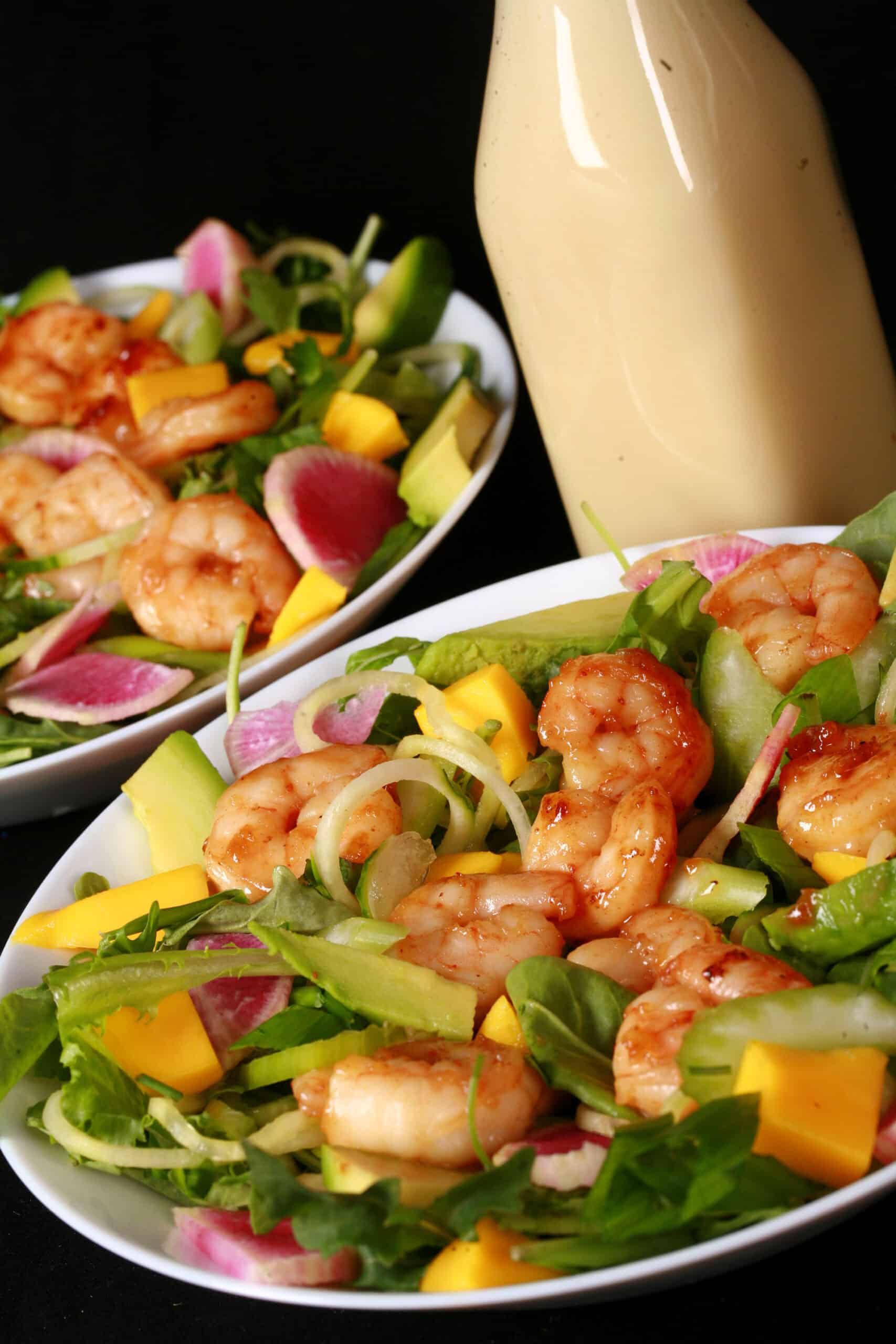 2 bowls of colourful calamansi glazed shrimp salad, with mangoes and a bottle of calamansi vinaigrette.