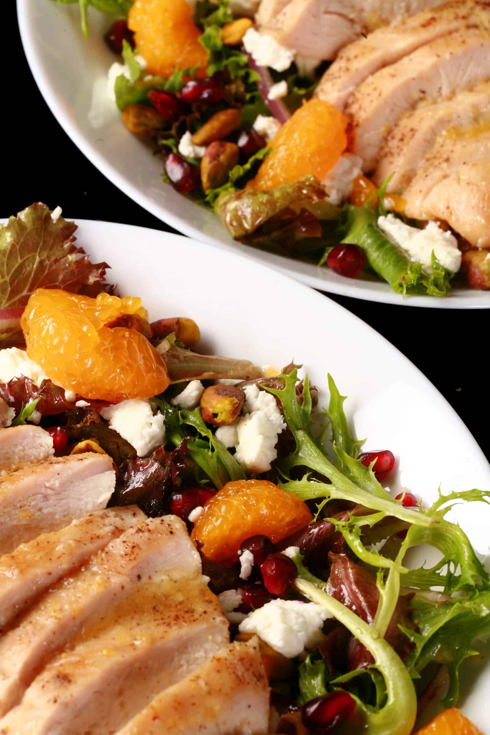 2 bowls of orange glazed chicken salad with mandarin orange segments, pomegranates, goat cheese, and pistachios.