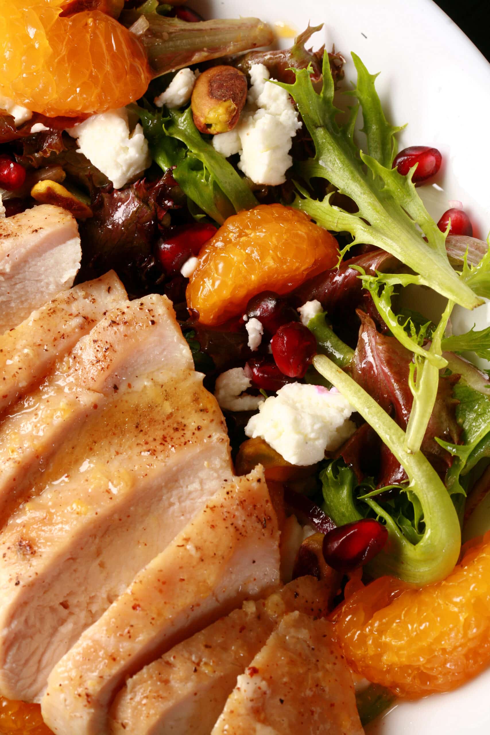 2 bowls of orange glazed chicken salad with mandarin orange segments, pomegranates, goat cheese, and pistachios.