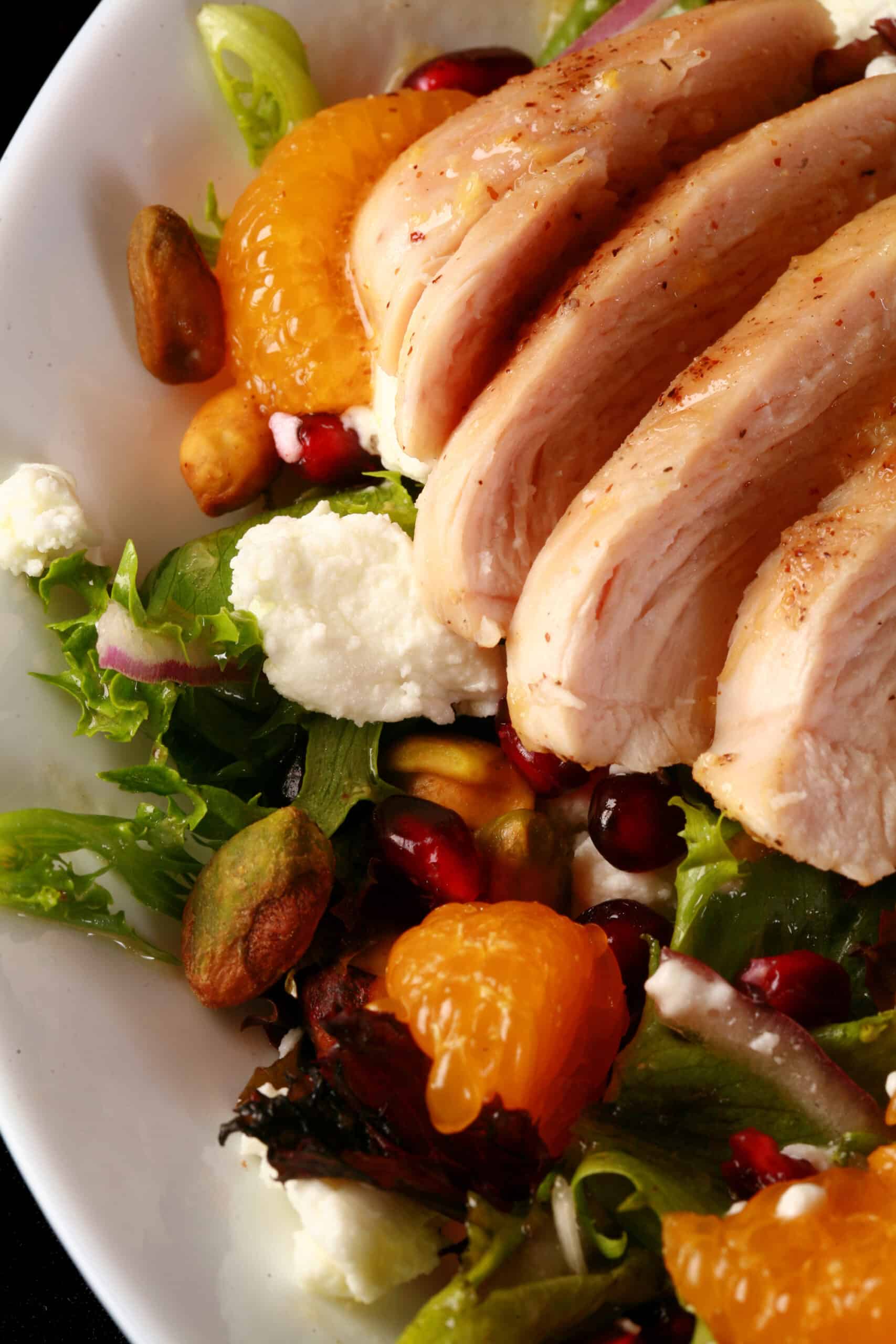 2 bowls of orange glazed chicken salad with mandarin orange segments, pomegranates, goat cheese, and pistachios.