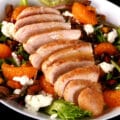 A bowl of Christmas salad with orange glazed chicken, mandarin orange segments, pomegranates, goat cheese, and pistachios.