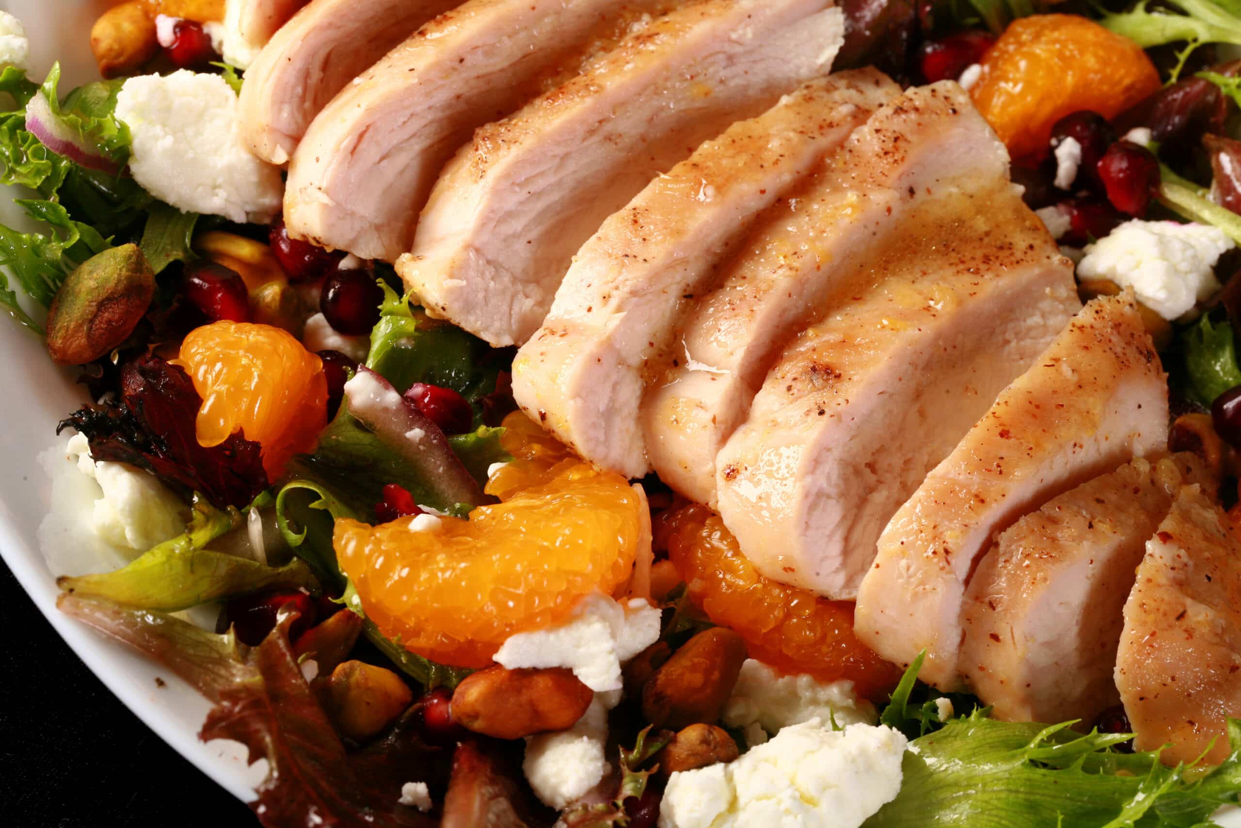 2 bowls of orange glazed chicken salad with mandarin orange segments, pomegranates, goat cheese, and pistachios.