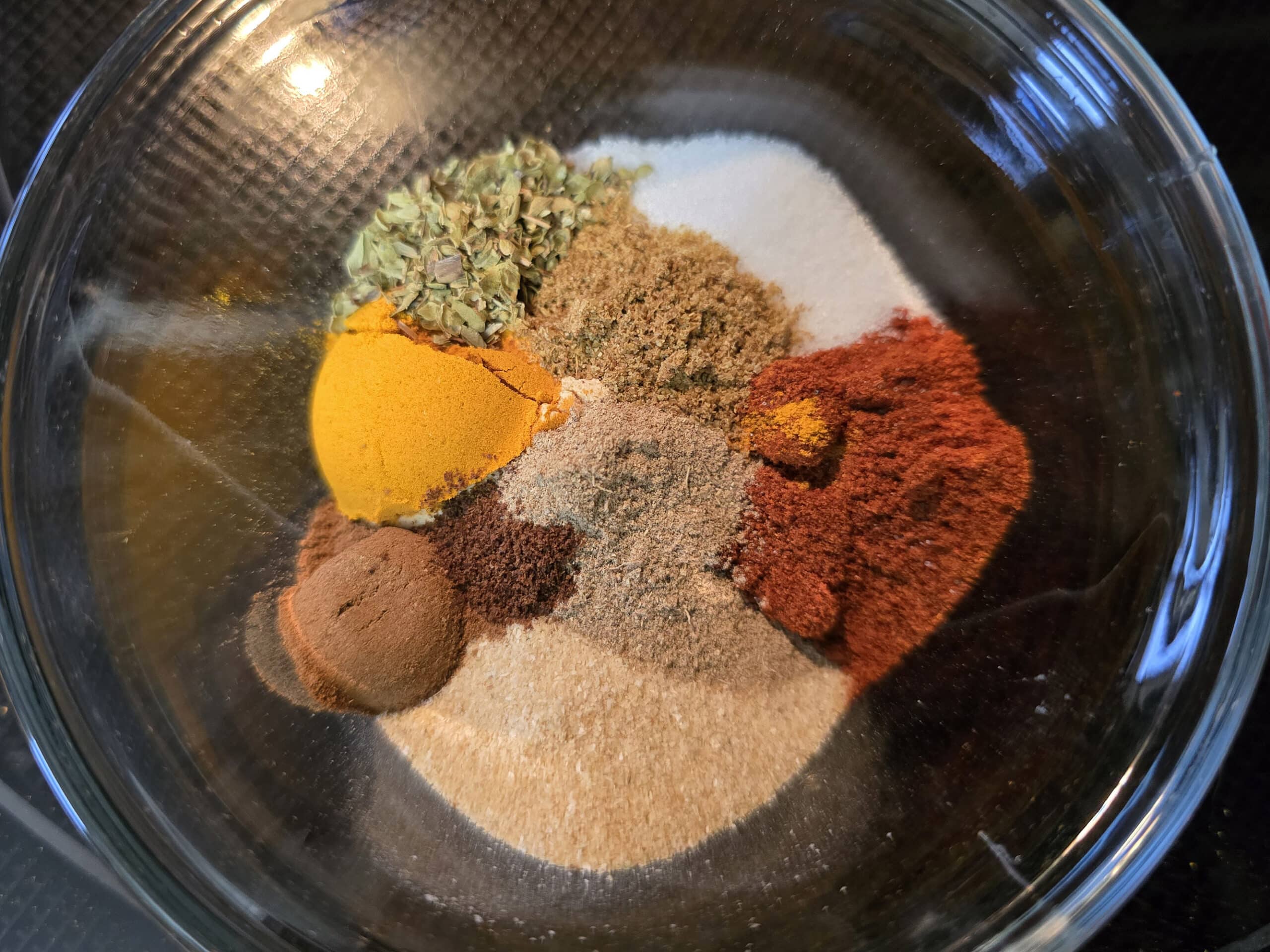 A small glass bowl with measured amounts of spices in it.