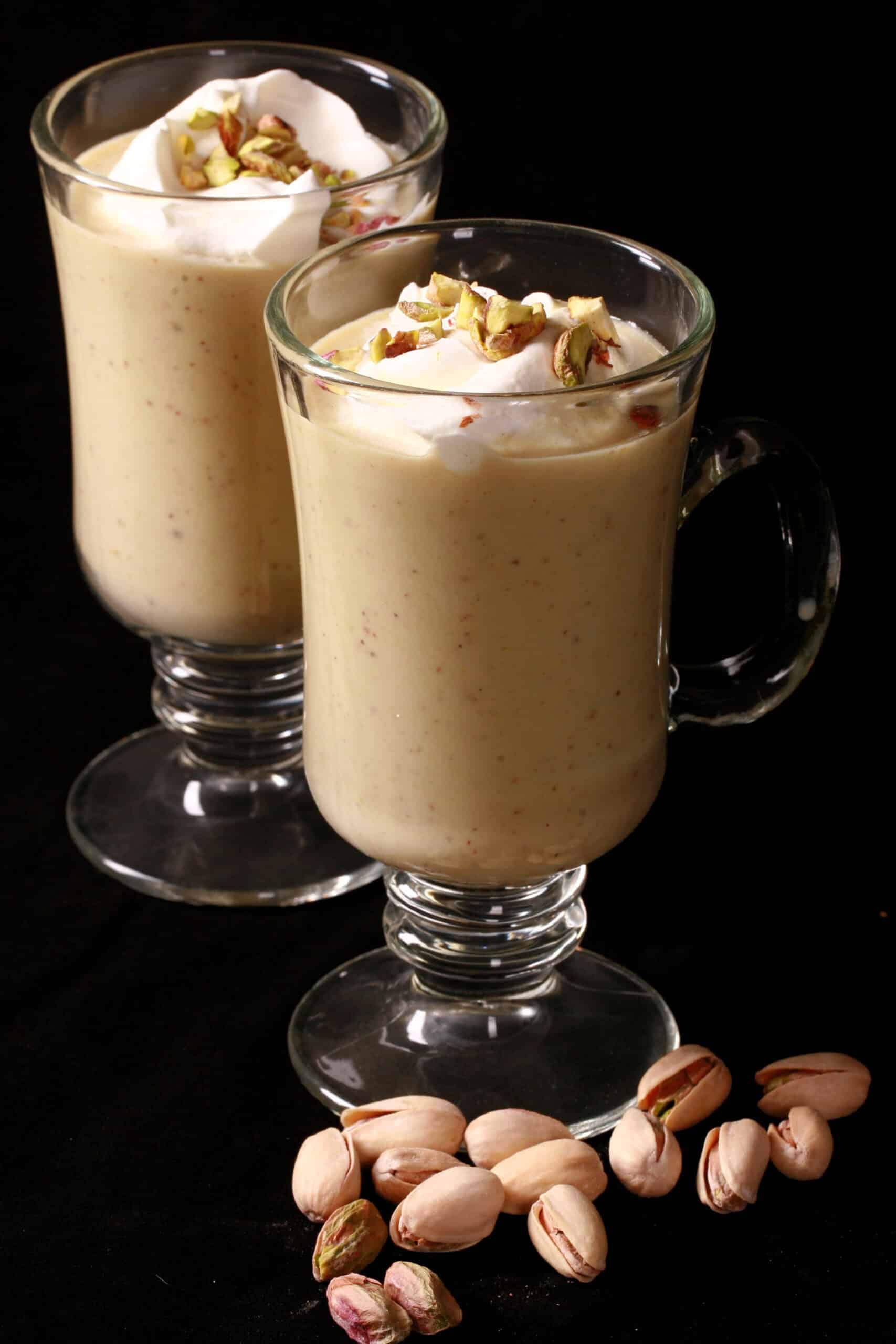 2 glass mugs of pistachio hot chocolate, topped with whipped cream and chopped pistachios.