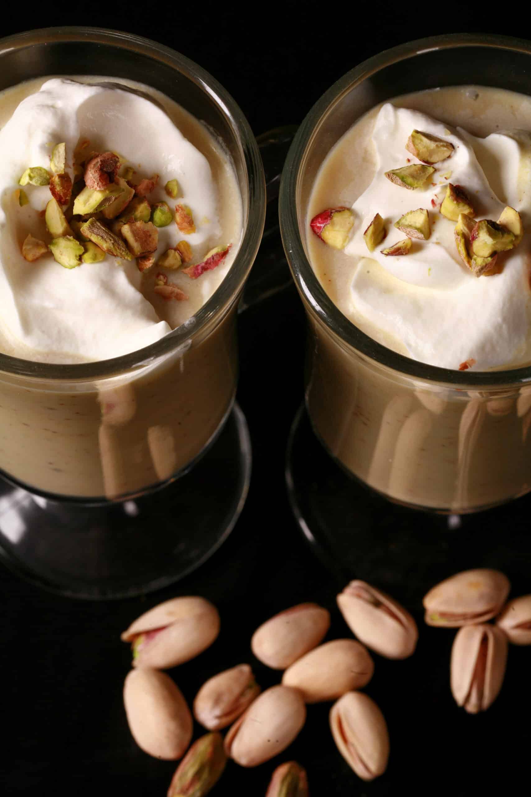 2 glass mugs of pistachio white hot chocolate, topped with whipped cream and chopped pistachios.