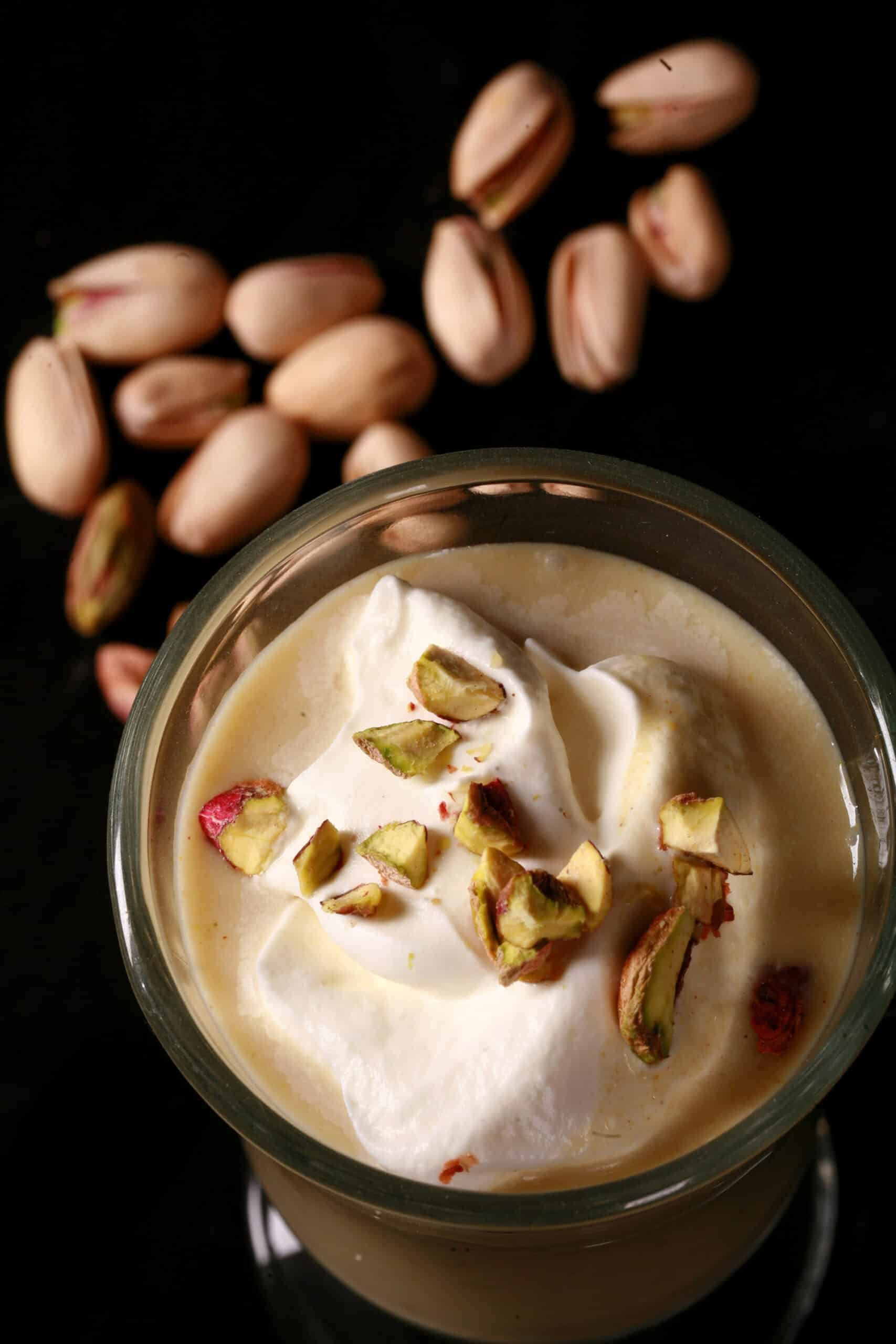 A glass mug of pistachio white hot chocolate, topped with whipped cream and chopped pistachios.