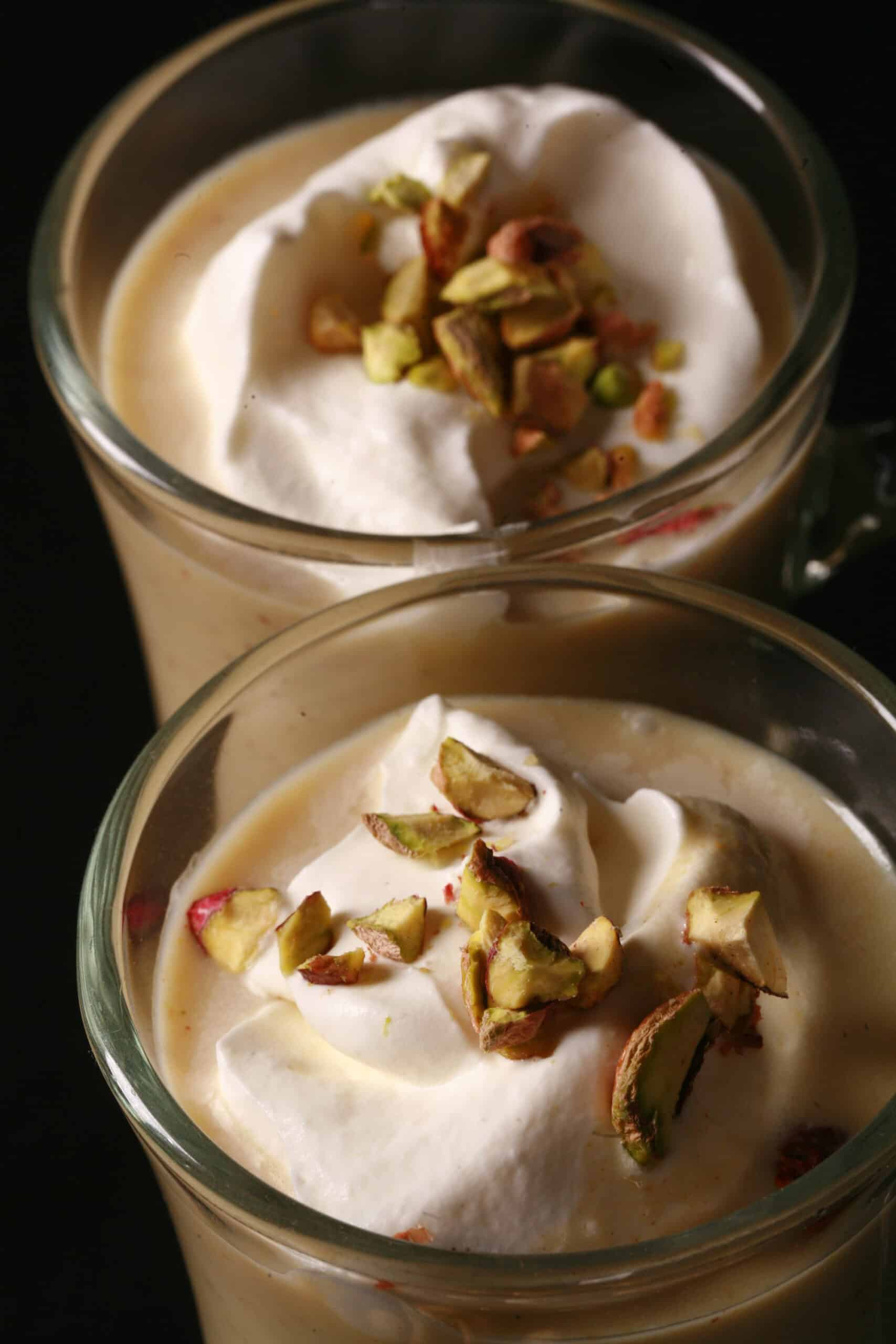 2 glass mugs of pistachio hot chocolate, topped with whipped cream and chopped pistachios.