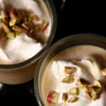 2 glass mugs of pistachio white hot chocolate, topped with whipped cream and chopped pistachios.