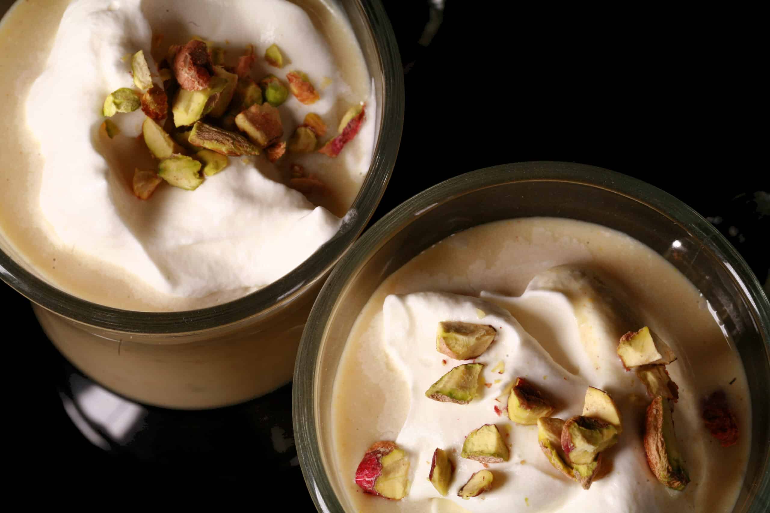 2 glass mugs of pistachio white hot chocolate, topped with whipped cream and chopped pistachios.