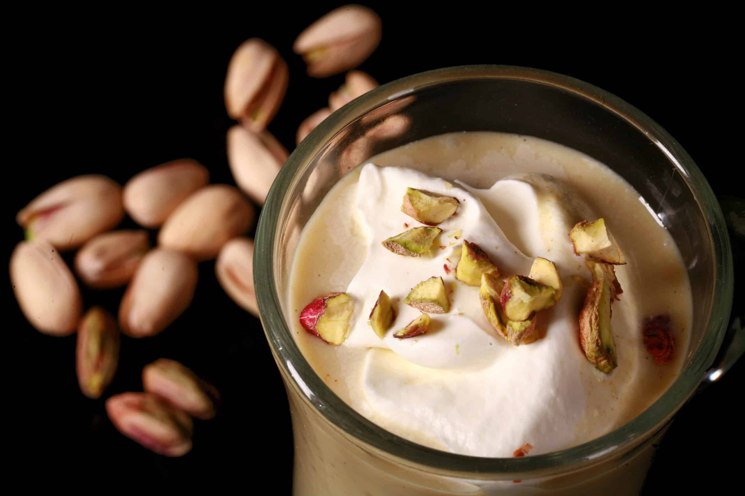 A glass mug of pistachio hot chocolate, topped with whipped cream and chopped pistachios.