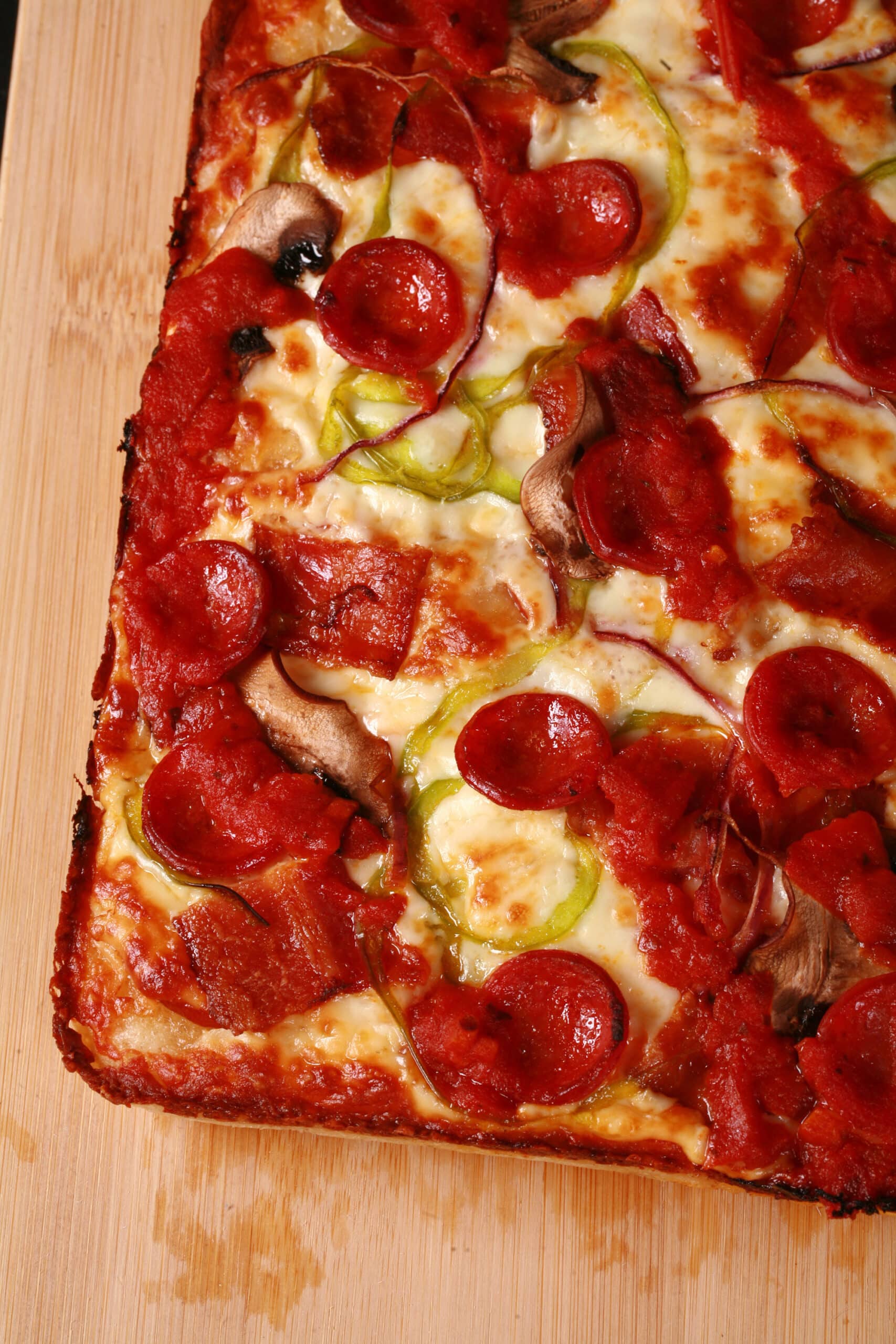 A cut slab of detroit style gluten free pizza with pepperoni, mushrooms, onion, bacon, and green peppers.