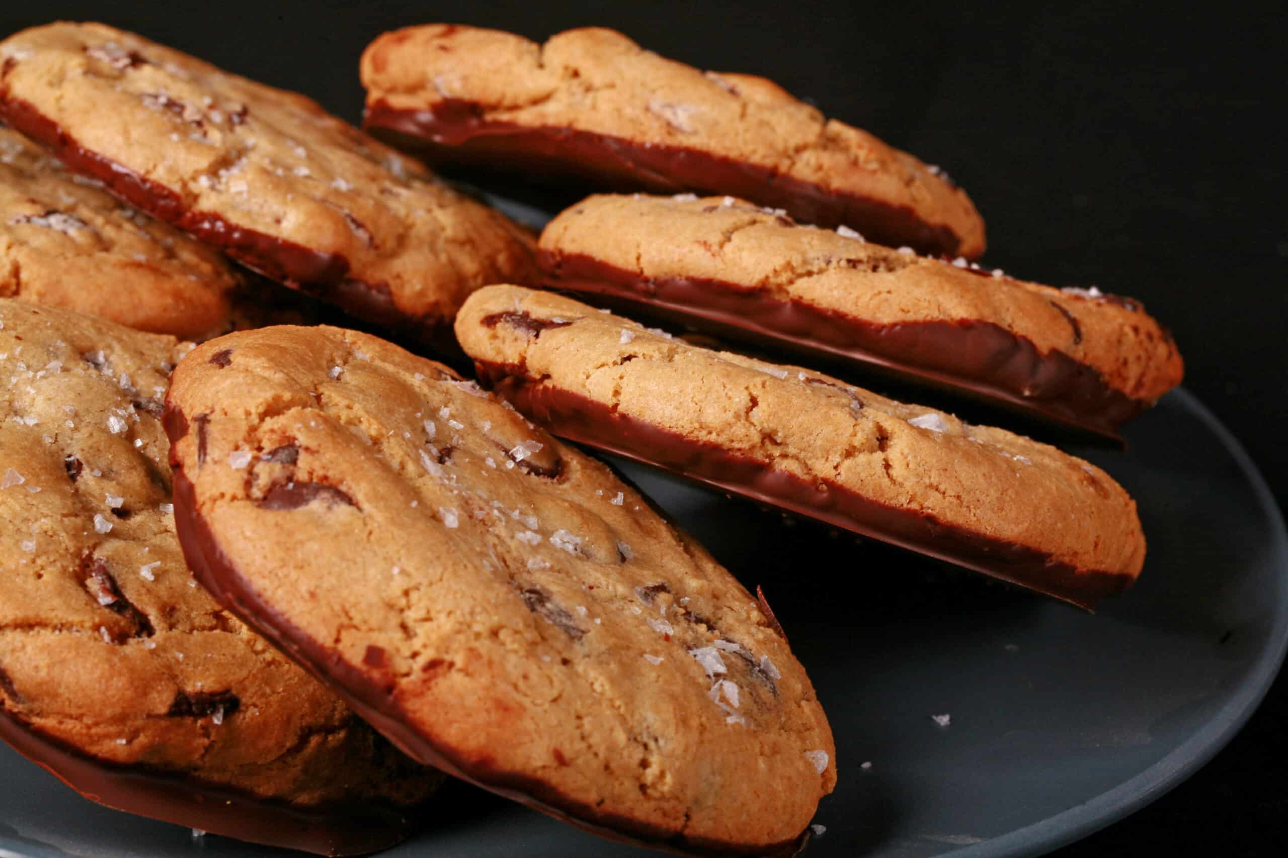 A plate of huge chocolate dipped gluten free jacques torres chocolate chip cookies sprinkled with sea salt.