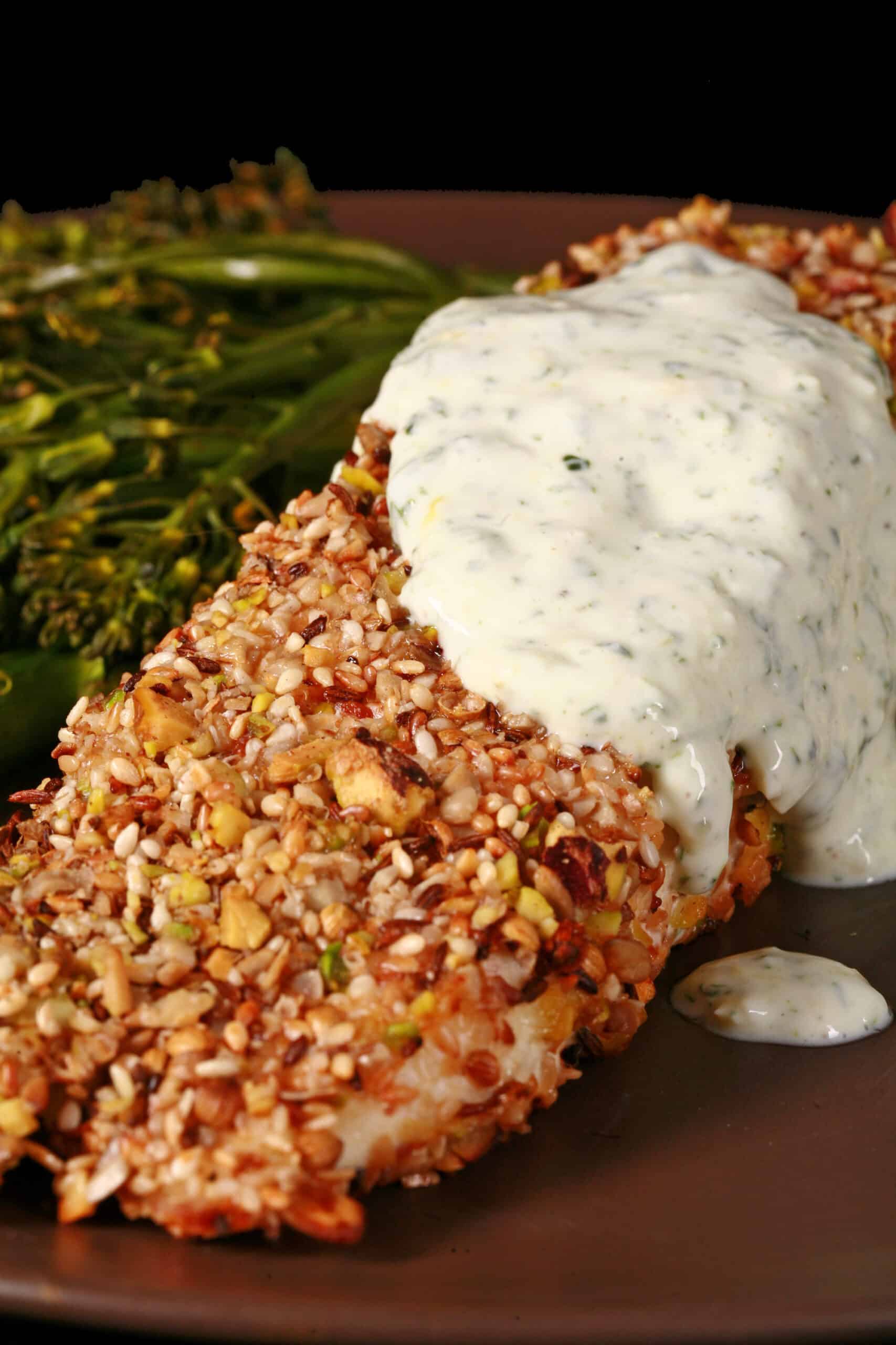 A plate of dukkah crusted baked halibut filet with lemon mint sauce and broccolini.