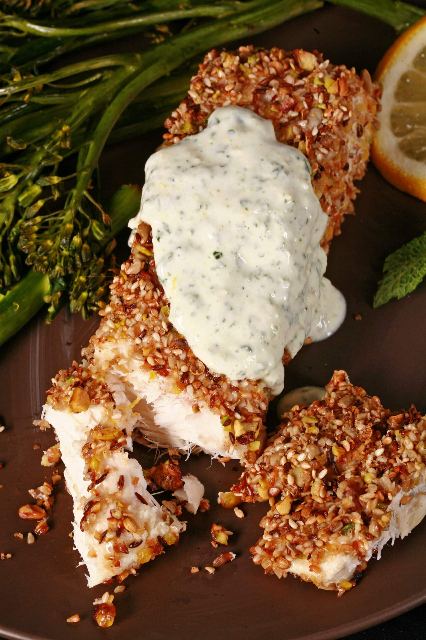 A plate of dukkah crusted baked halibut filet with lemon mint sauce and broccolini.
