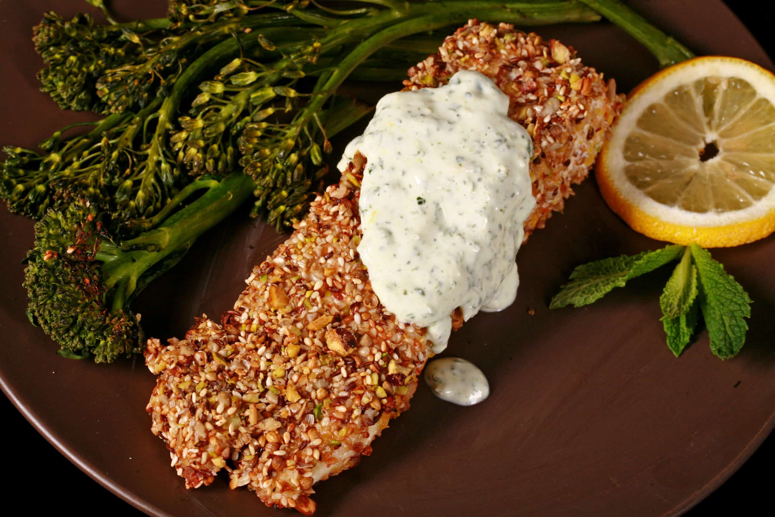 A plate of dukkah crusted baked halibut filet with lemon mint sauce and broccolini.