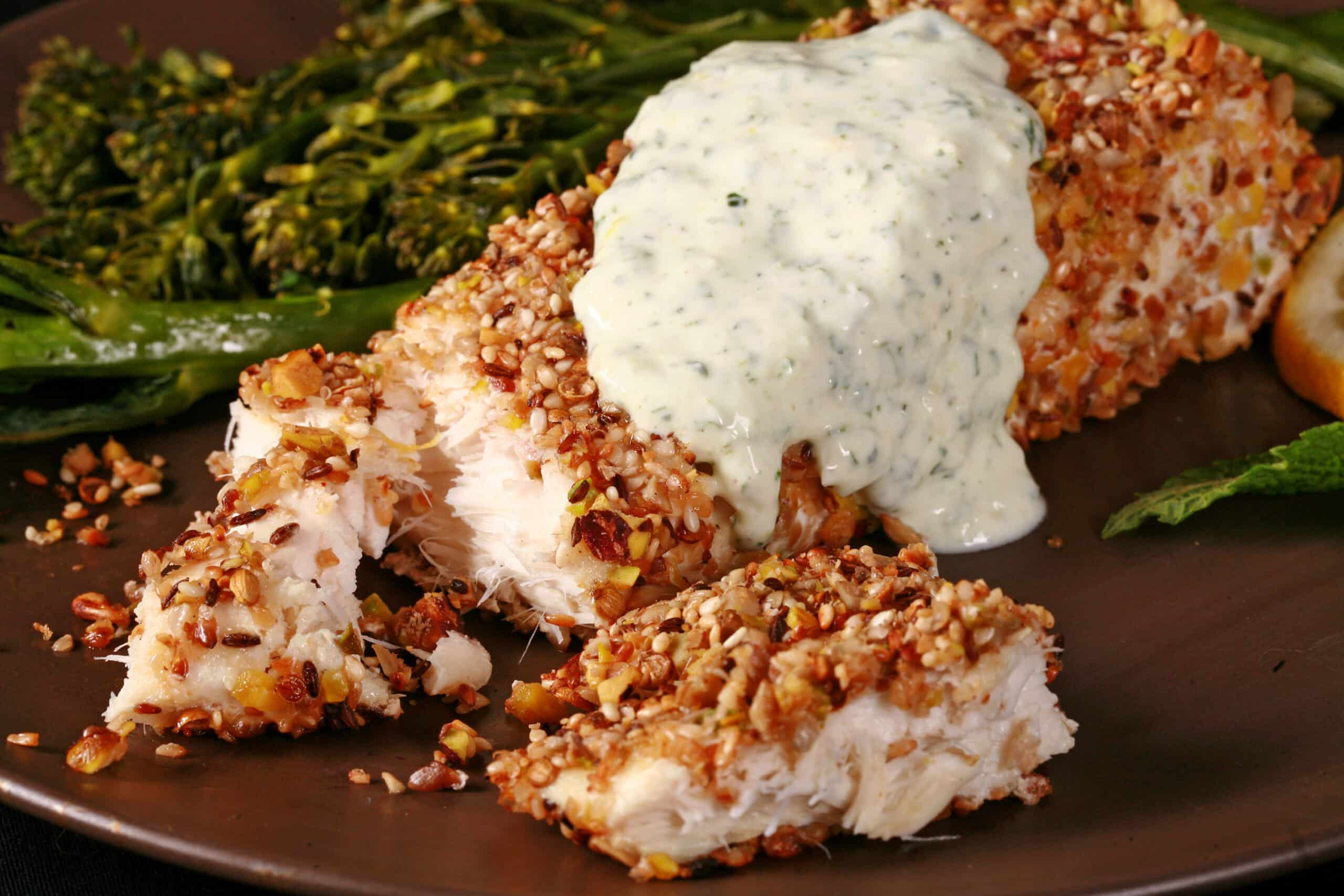A plate of dukkah crusted halibut filet with lemon mint sauce and broccolini.