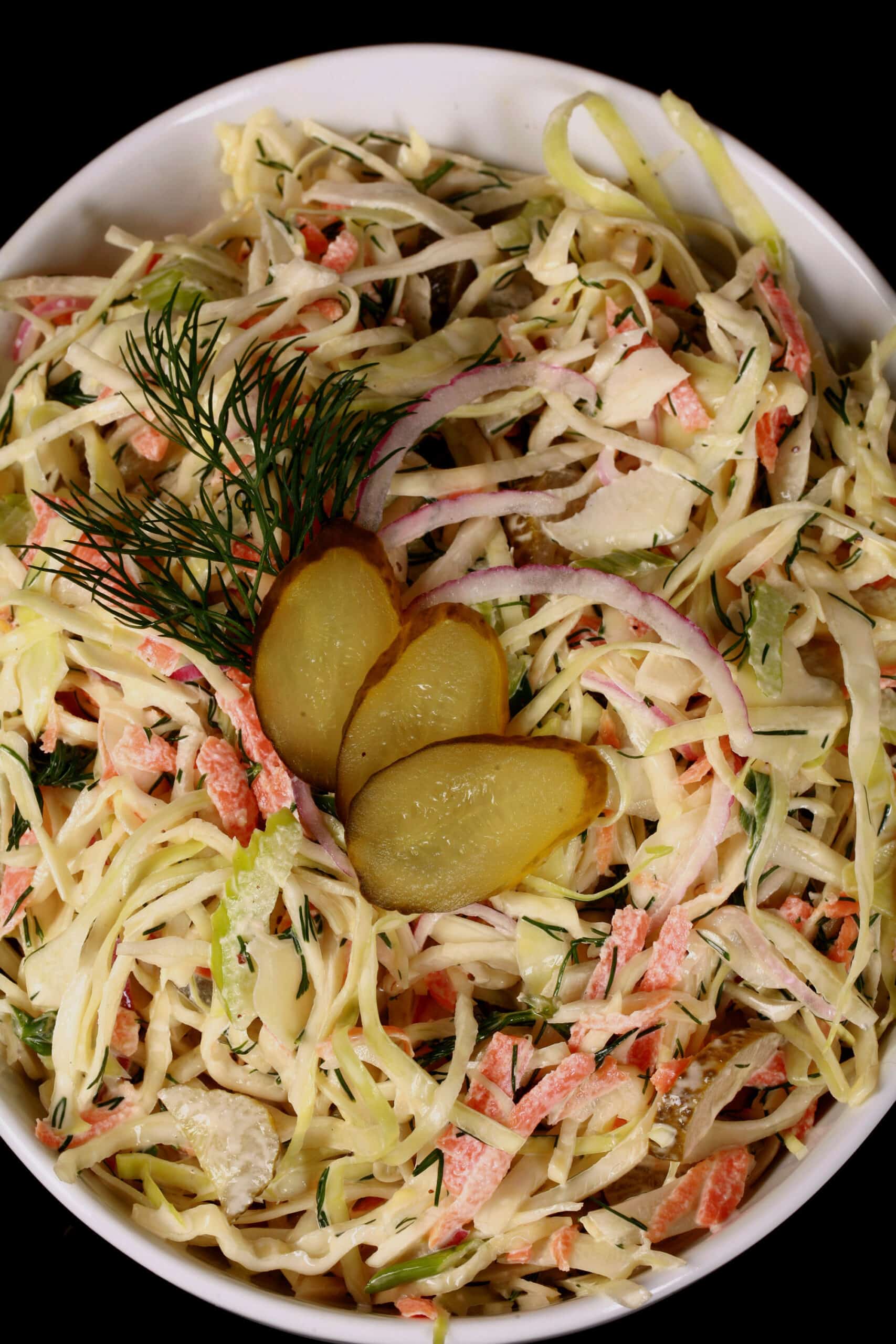 A bowl of creamy coleslaw with cabbage, carrots, red onions, pickles, and more.