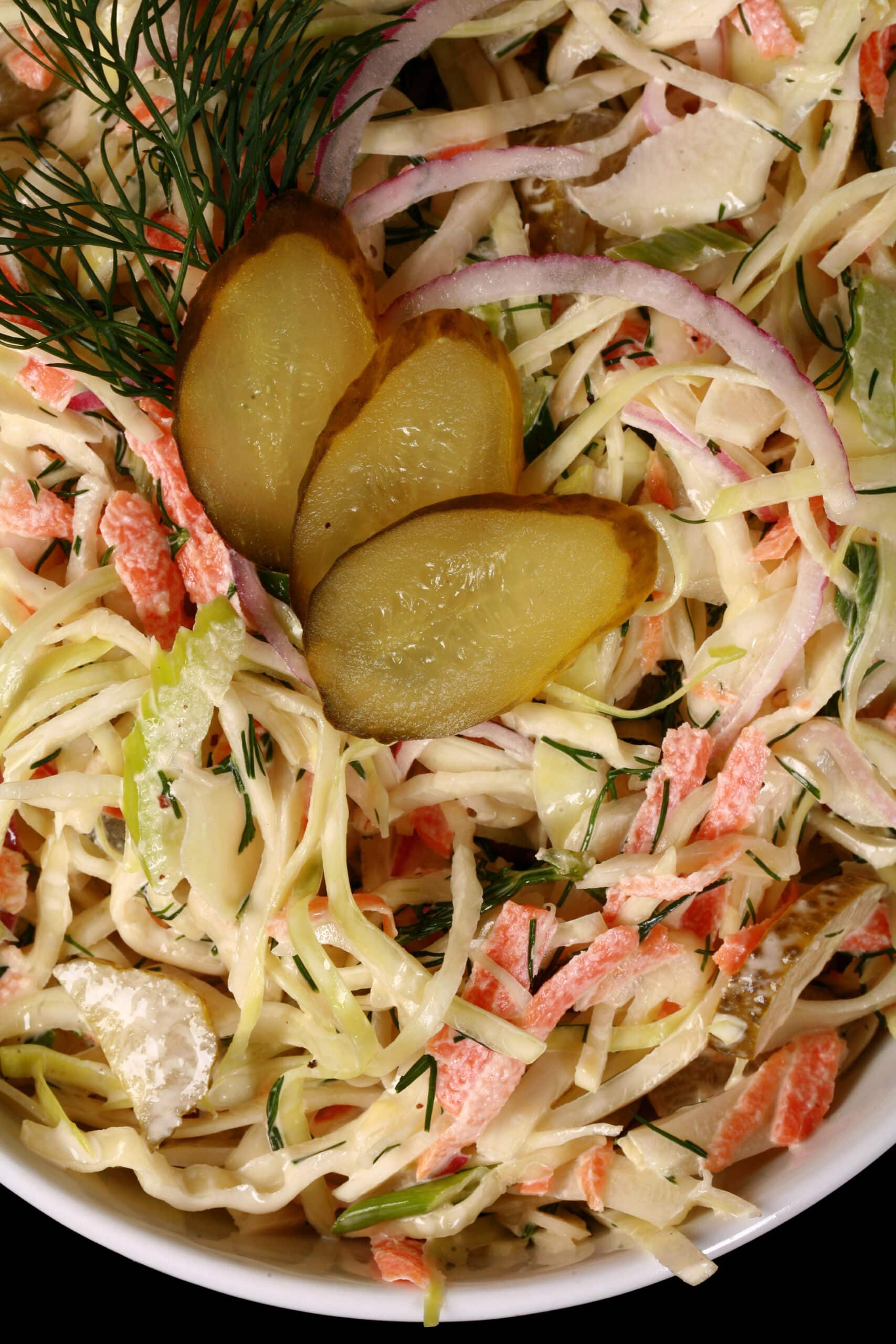 A bowl of creamy dill pickle coleslaw with cabbage, carrots, red onions, pickles, and more.