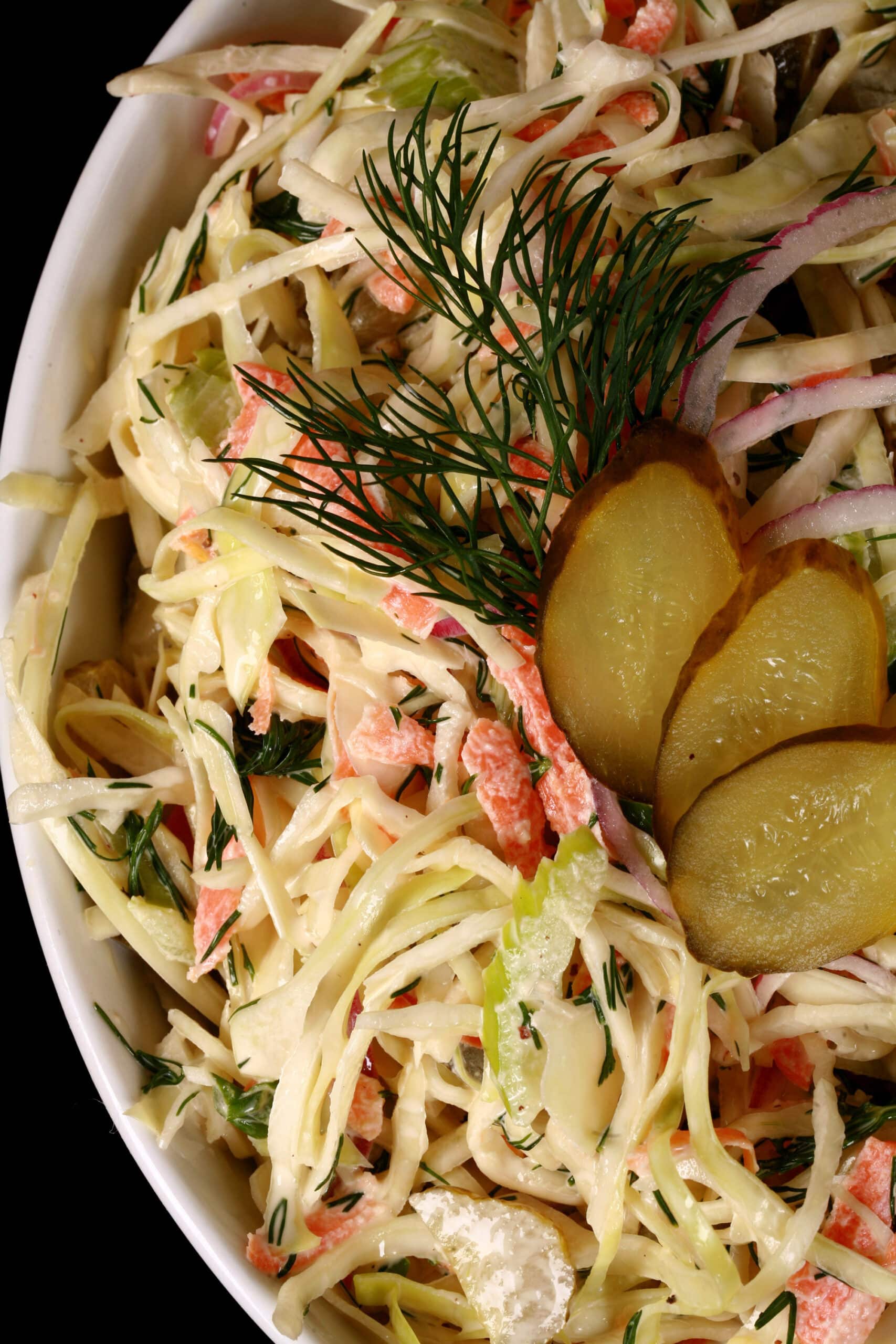 A bowl of creamy coleslaw with cabbage, carrots, red onions, pickles, and more.