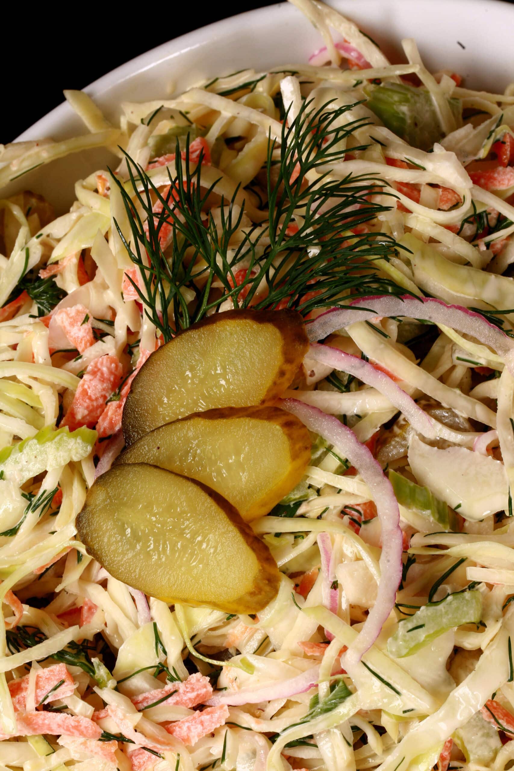 A bowl of creamy dill pickle coleslaw with cabbage, carrots, red onions, pickles, and more.