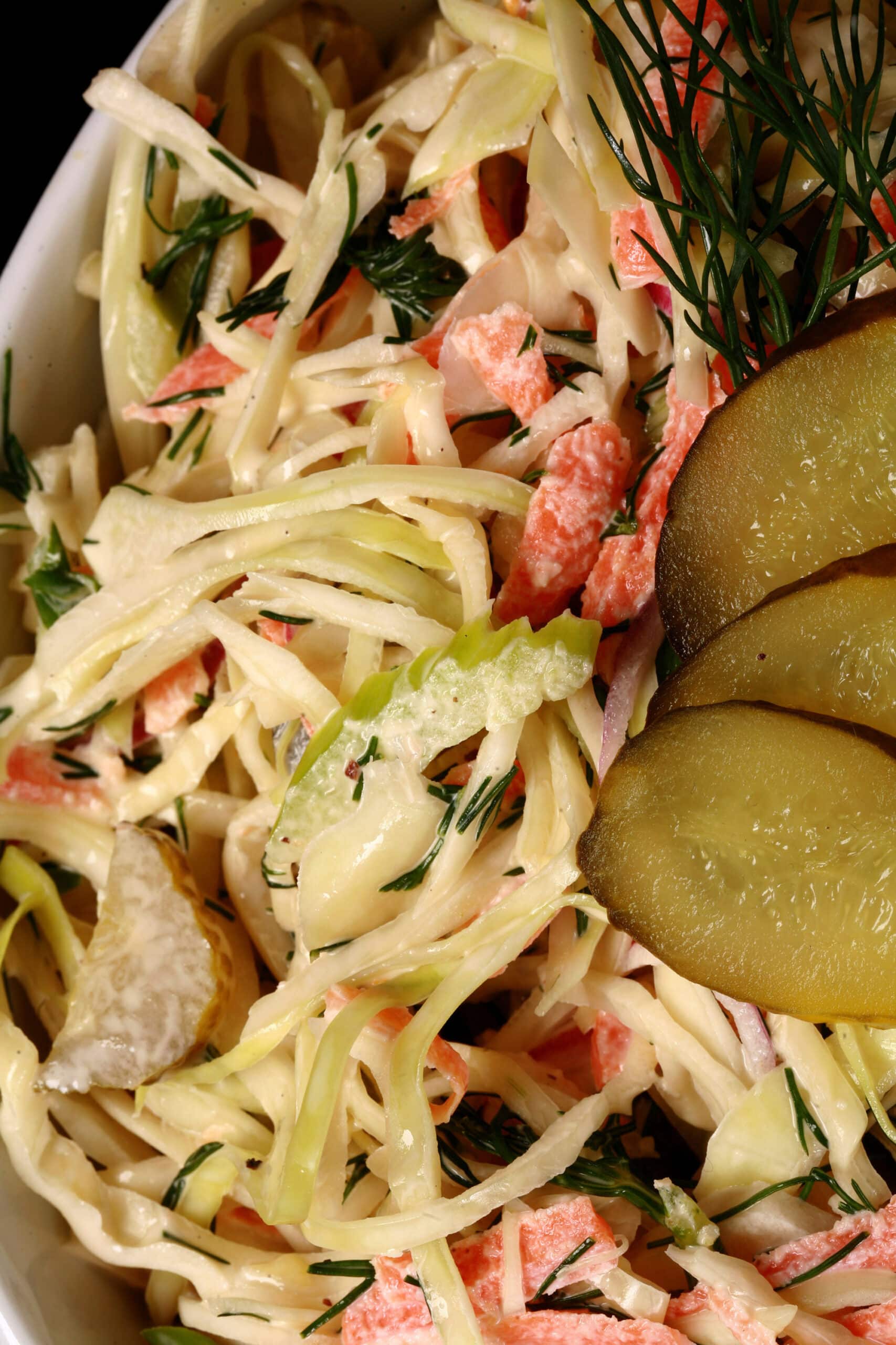 A bowl of creamy coleslaw with cabbage, carrots, red onions, pickles, and more.