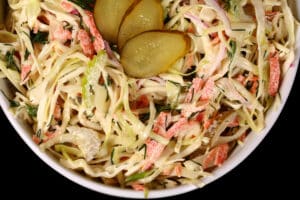 A bowl of creamy dill pickle coleslaw with cabbage, carrots, red onions, pickles, and more.