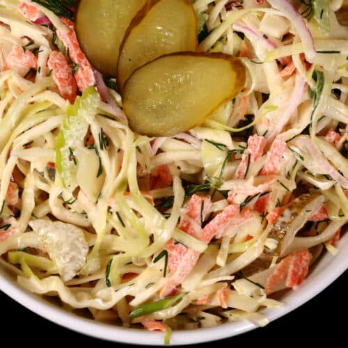 A bowl of creamy dill pickle coleslaw with cabbage, carrots, red onions, pickles, and more.