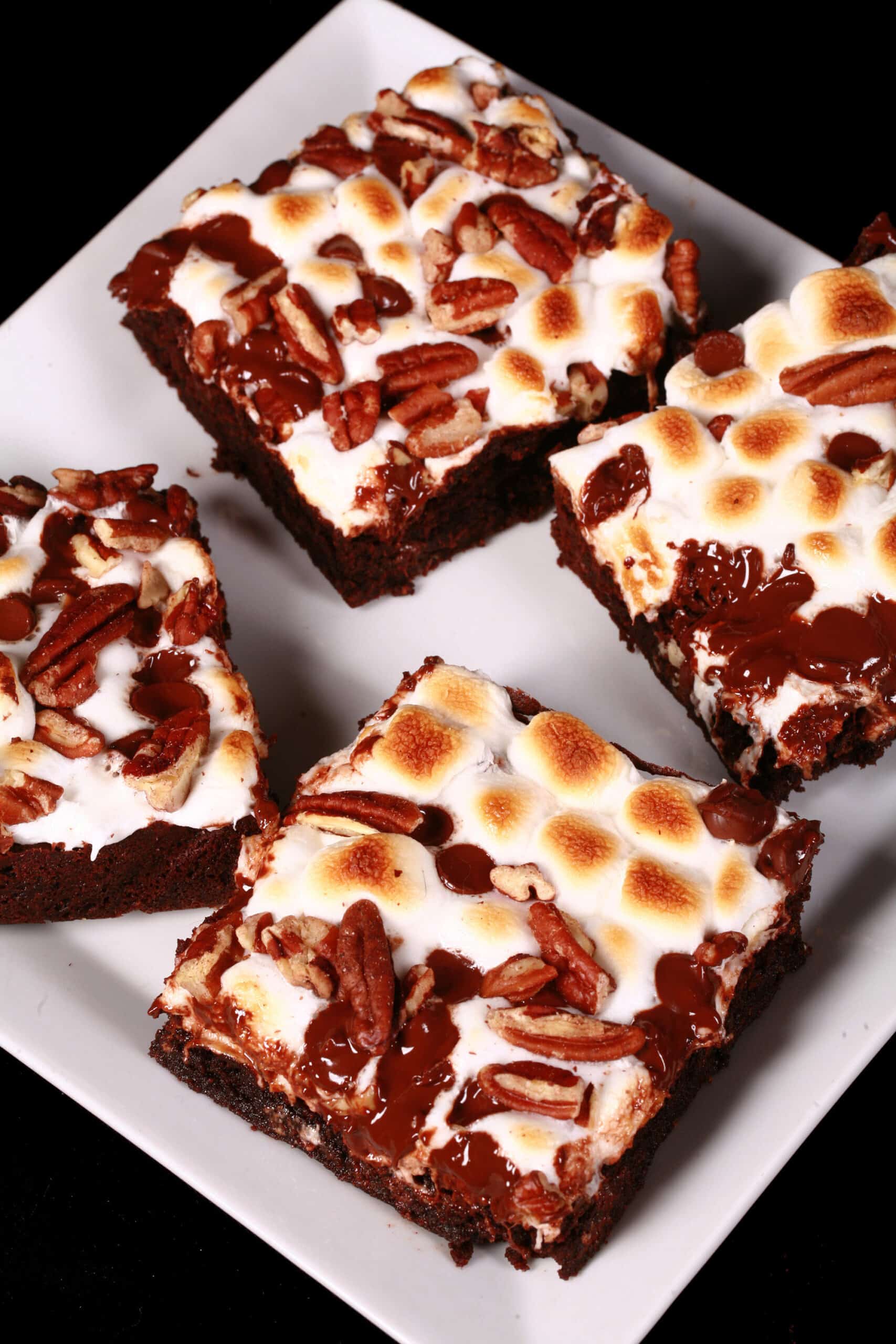 A plate of gluten free rocky road brownies, topped with toasted mini marshmallows, pecans, and chocolate chips.