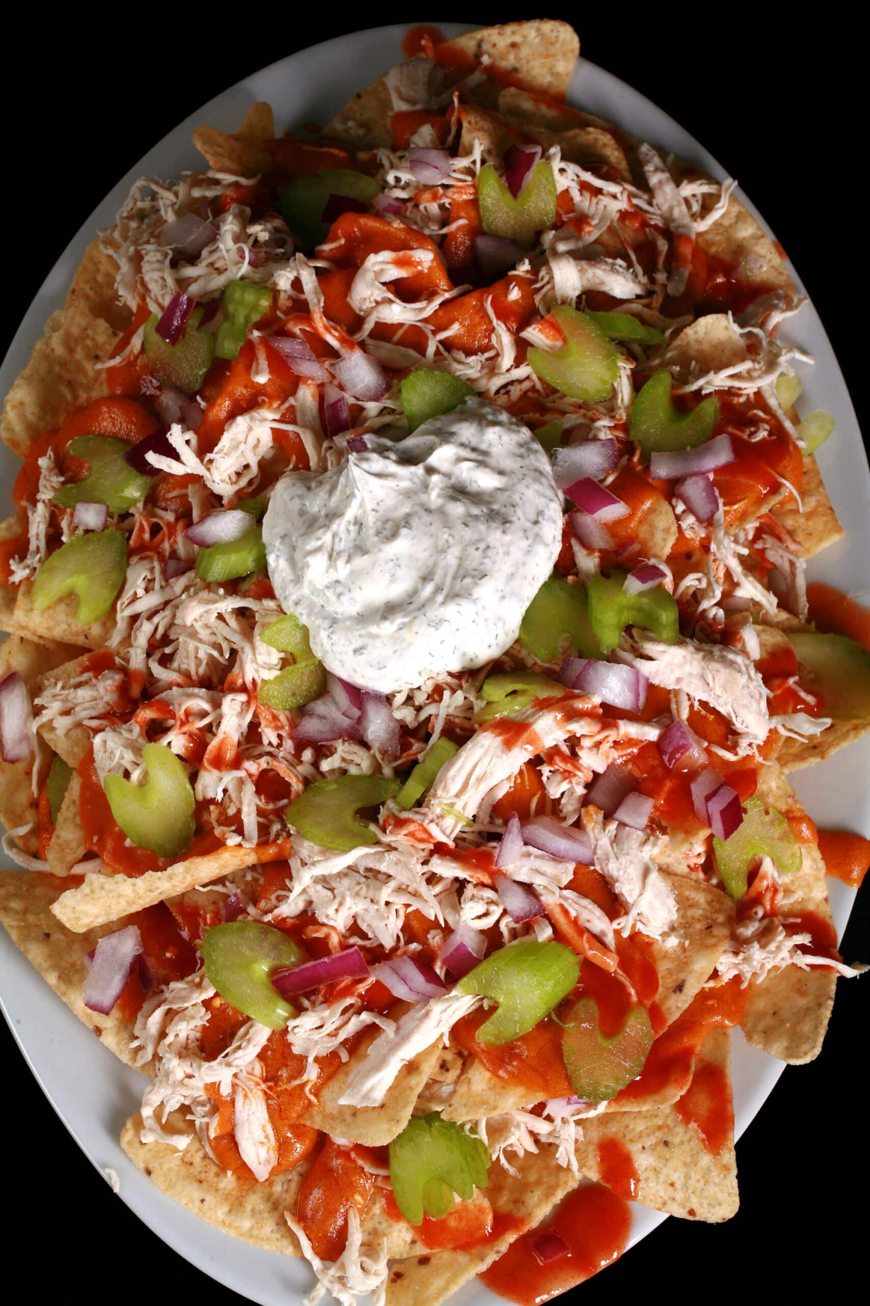 A platter of buffalo wing nachos, with shredded chicken, Buffalo Wing nacho cheese sauce, hot sauce, red onions, celery, and ranch flavoured sour cream.