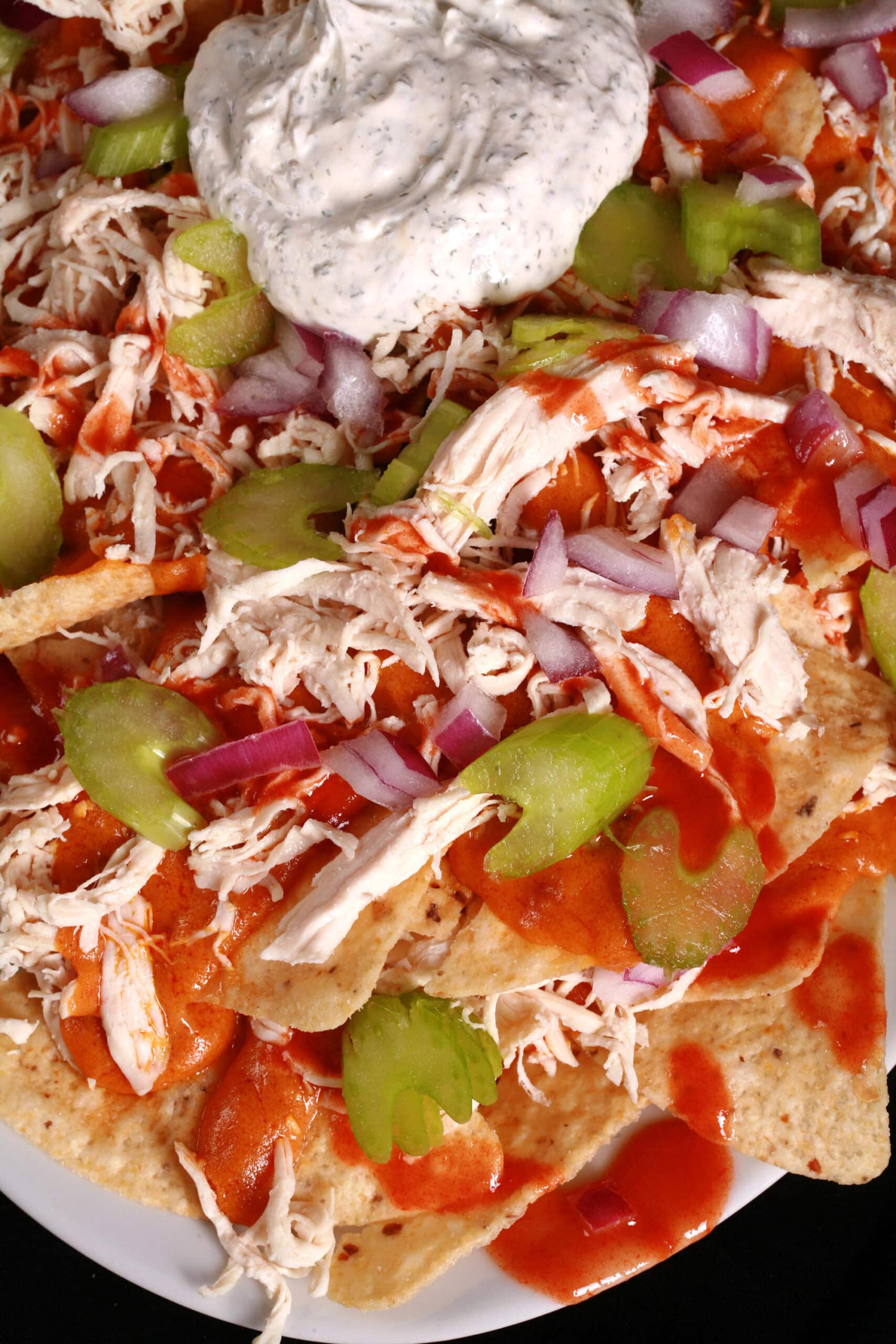 A platter of buffalo wing nachos, with shredded chicken, Buffalo Wing nacho cheese sauce, hot sauce, red onions, celery, and ranch flavoured sour cream.