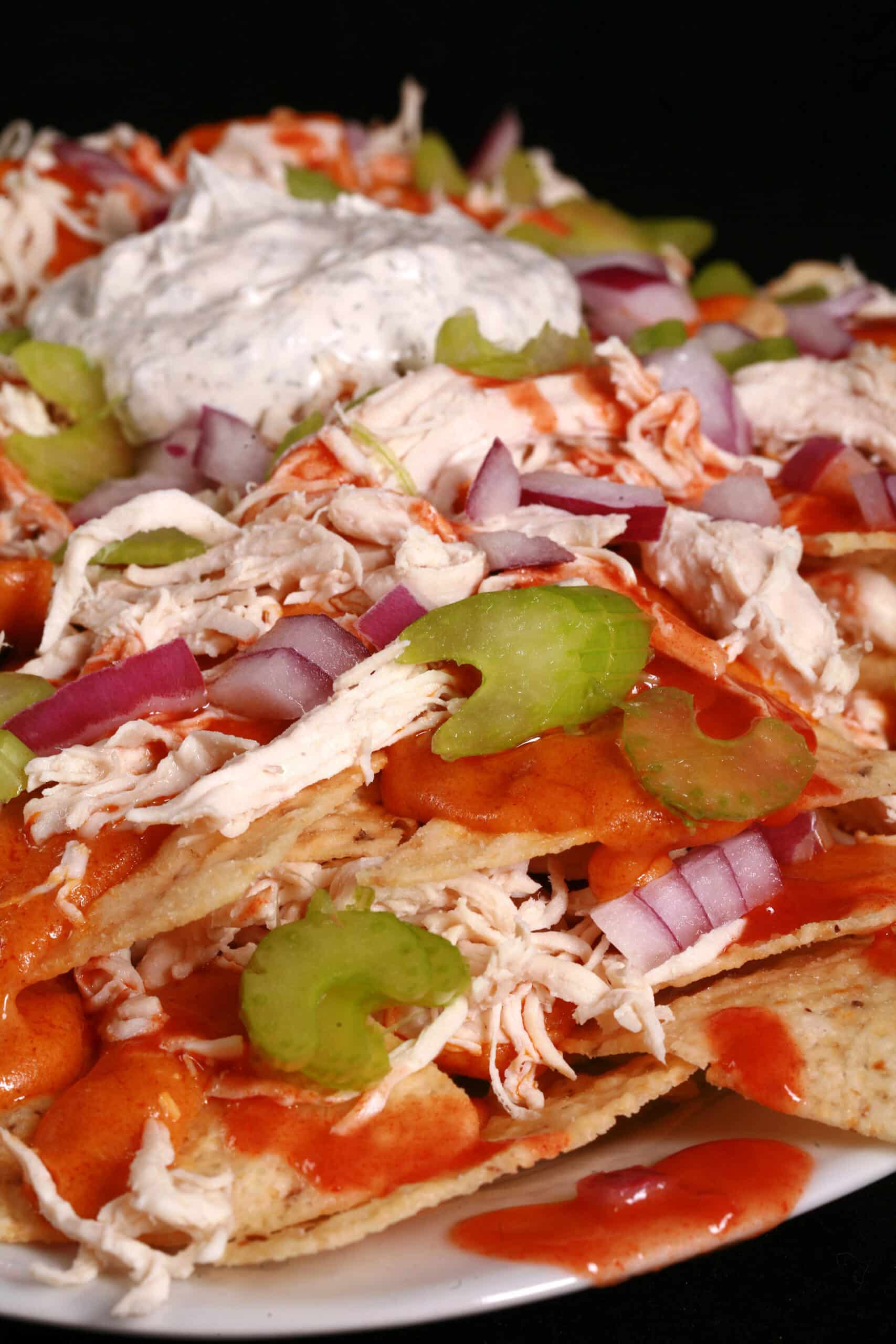 A platter of buffalo chicken nachos, with shredded chicken, Buffalo Wing nacho cheese sauce, hot sauce, red onions, celery, and ranch flavoured sour cream.