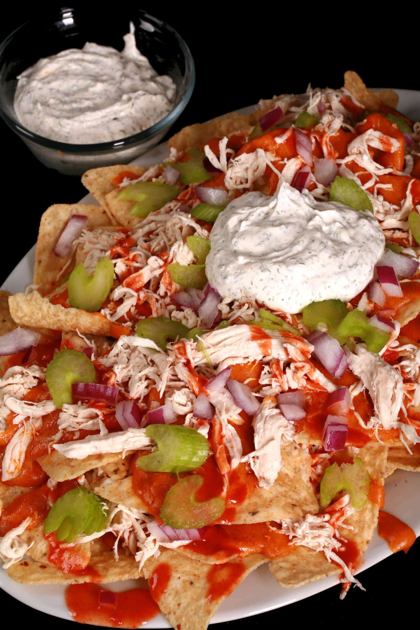 A platter of buffalo wing nachos, with shredded chicken, Buffalo Wing nacho cheese sauce, hot sauce, red onions, celery, and ranch flavoured sour cream.