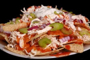 A platter of buffalo chicken nachos, with shredded chicken, Buffalo Wing nacho cheese sauce, hot sauce, red onions, celery, and ranch flavoured sour cream.
